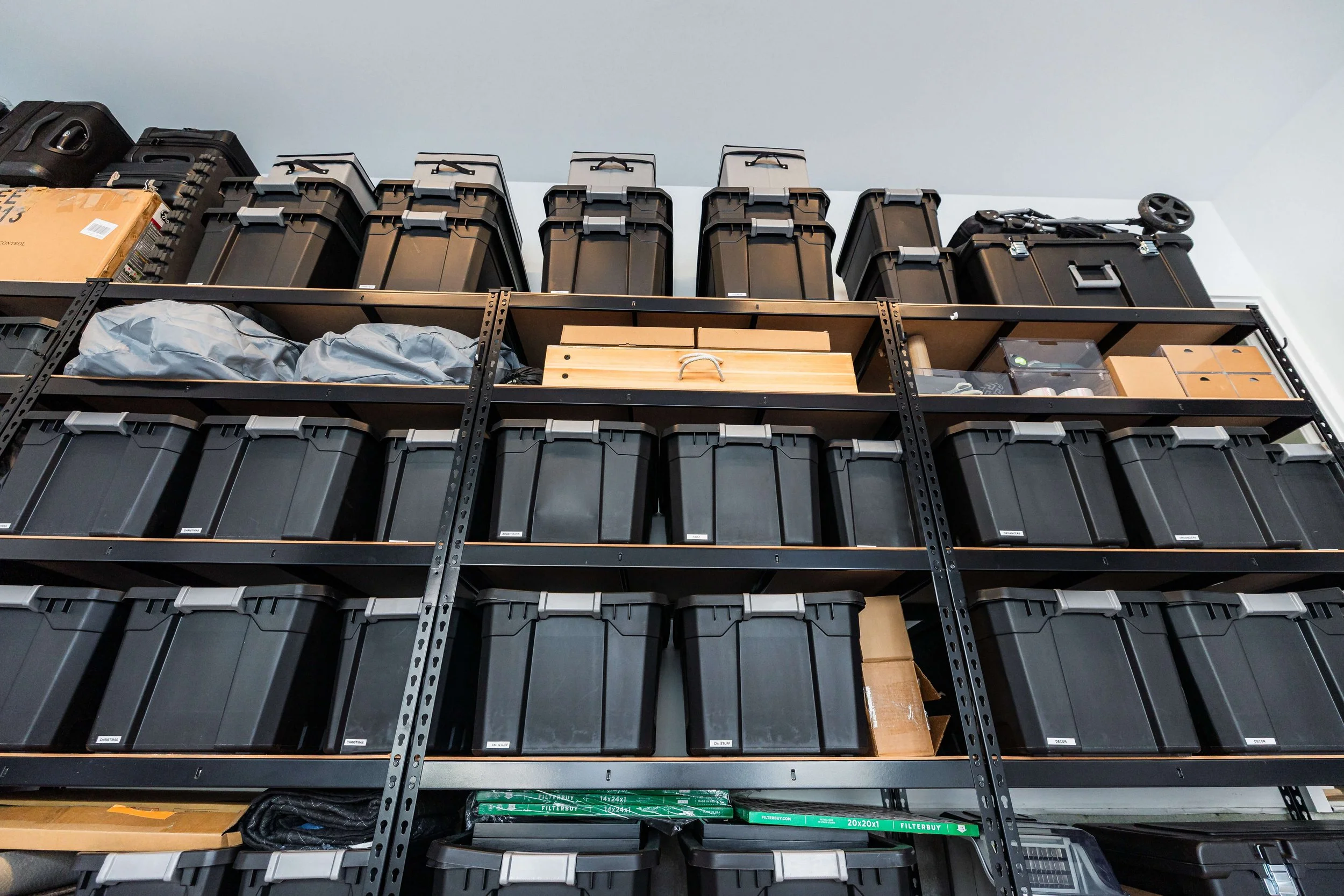 Labeled black storage bins arranged on garage shelves for organized storage.