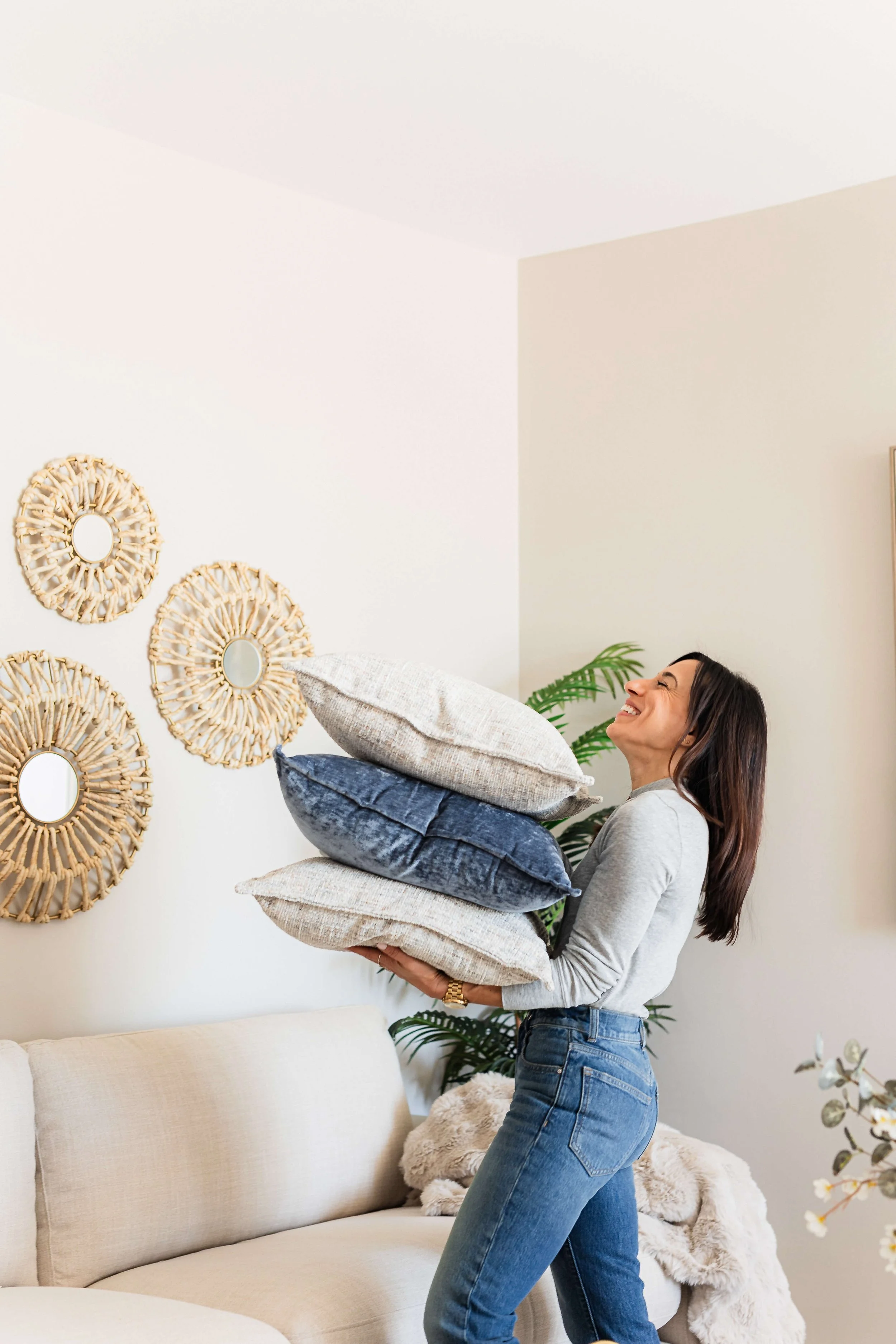 Designer carrying pillows through a hotel-inspired coastal living room during a relaxed, behind-the-scenes design moment.