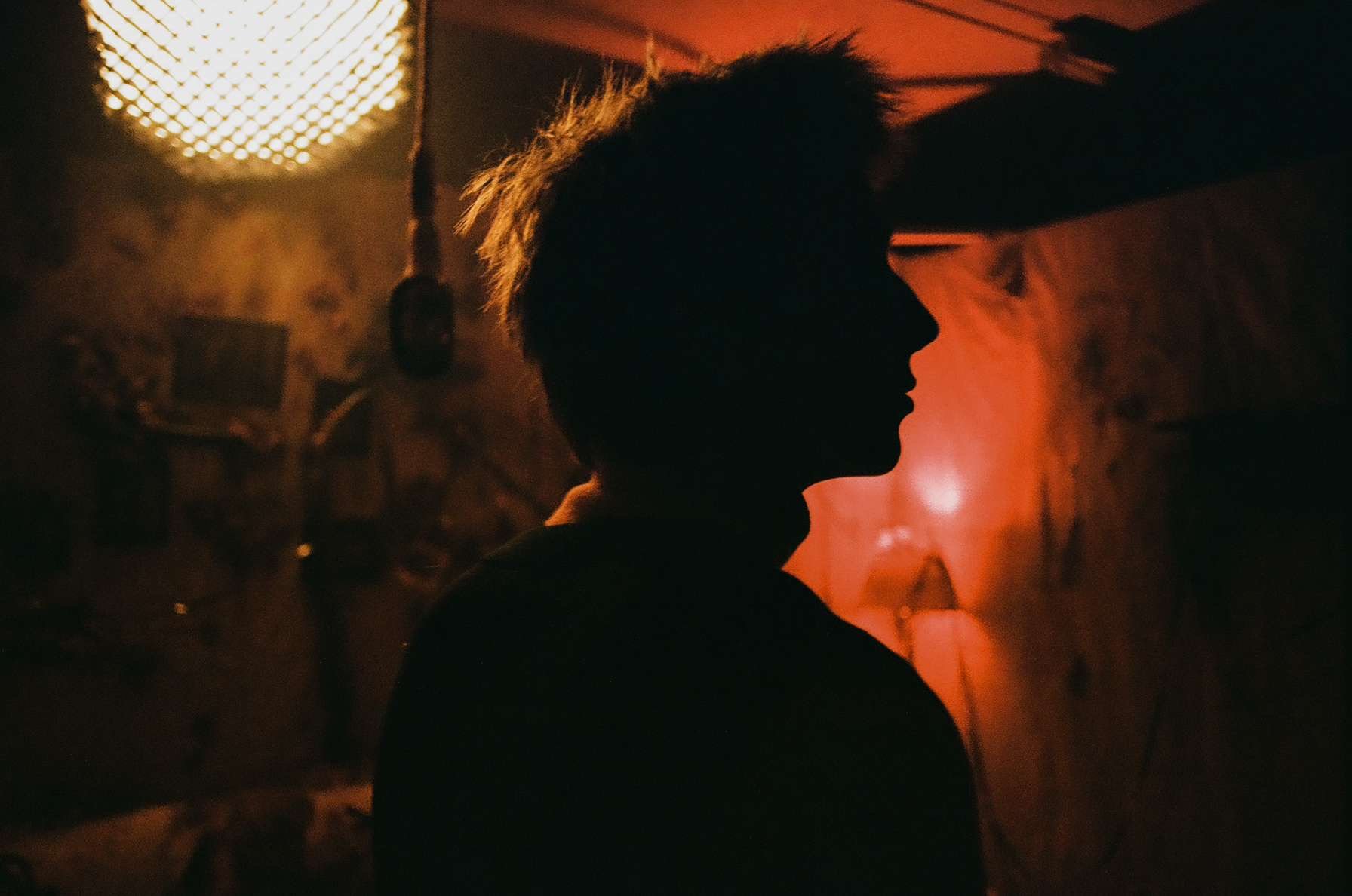 Silhouette of a person with spiky hair against dim, warm lighting indoors.