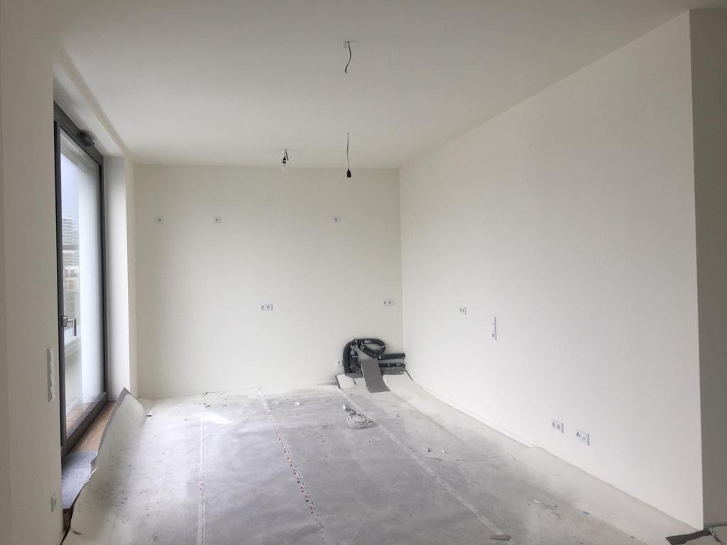 Empty room under renovation with bare walls, unfinished floor, exposed wiring, and a large window on one side.