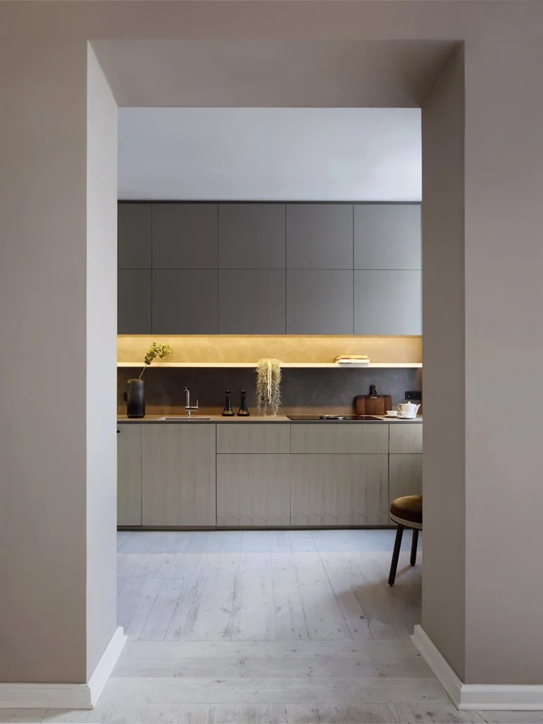 Modern kitchen with gray cabinets, a wooden countertop, and minimal decor, viewed through a doorway.