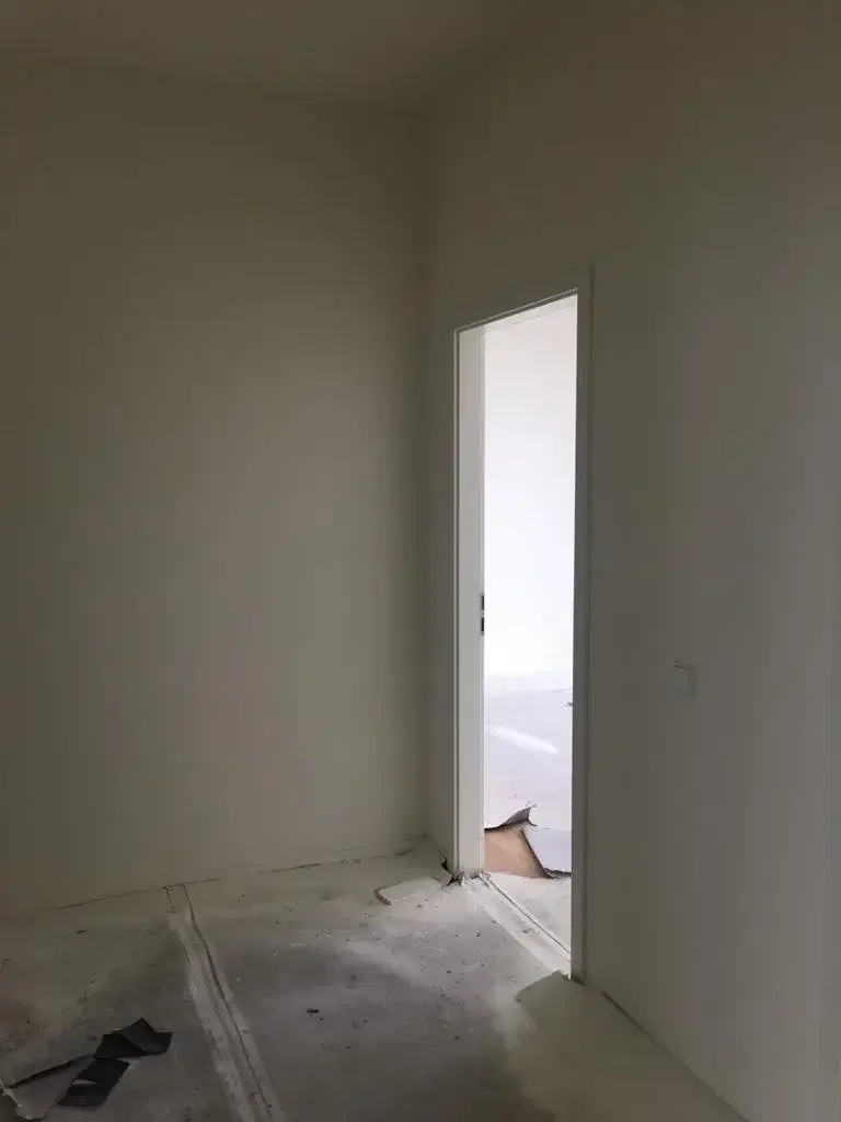 Empty room with an open door leading to another room with light coming through, construction debris on the floor.