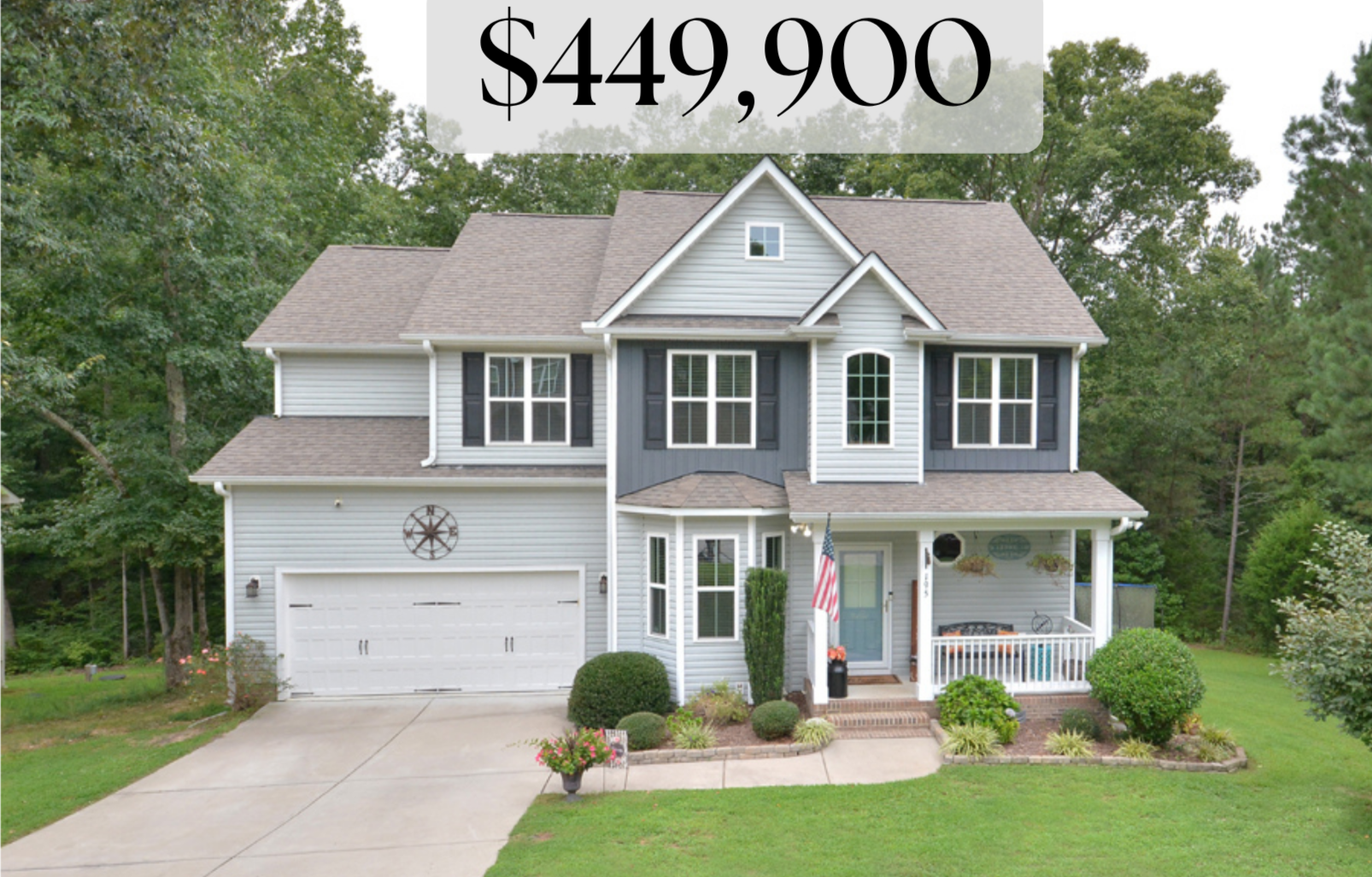 Front view of a two-story suburban house with a gray and blue exterior, white trim, a two-car garage, and a small front porch adorned with plants and an American flag.