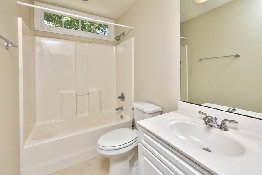 Bathroom with bathtub, toilet, and sink with mirror. Small window above bathtub, towel rack on wall.