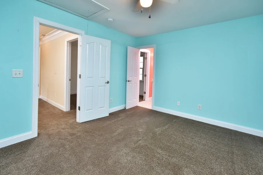 Empty room with light blue walls, brown carpet, and two white open doors leading to different rooms.