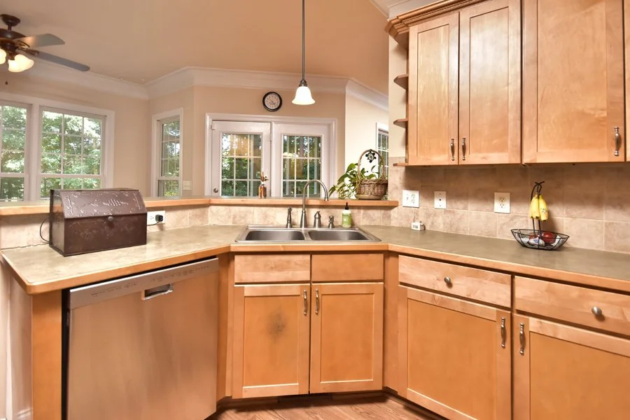 Kitchen with wooden cabinets, beige countertops, stainless steel sink, dishwasher, and large windows in the background.