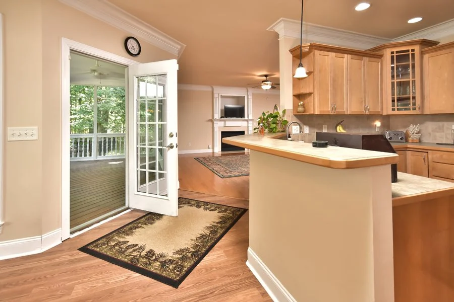 Open kitchen and living room area with wooden cabinets, a balcony door, a fireplace, and a ceiling fan.