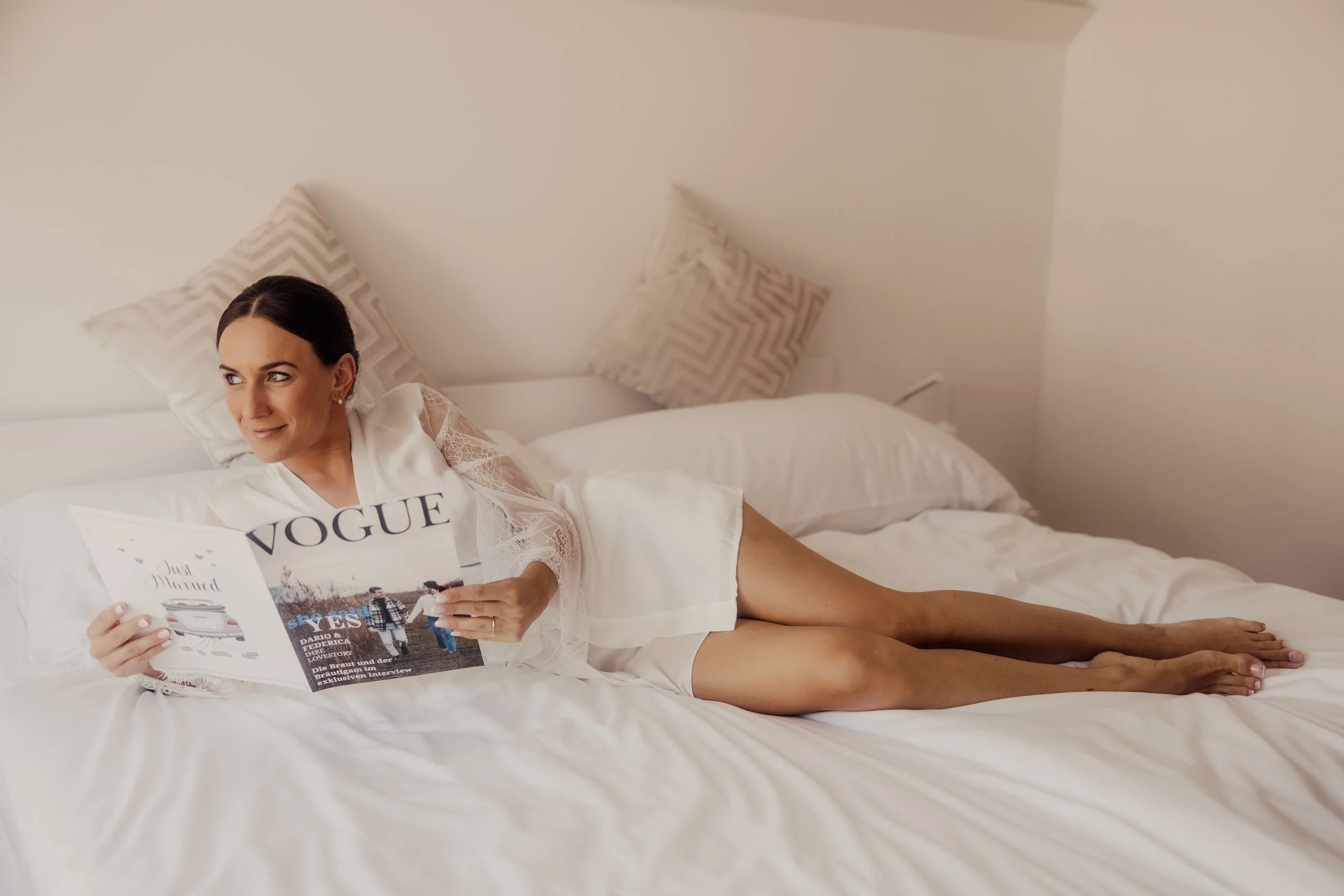 Woman lounging on a bed reading Vogue magazine.