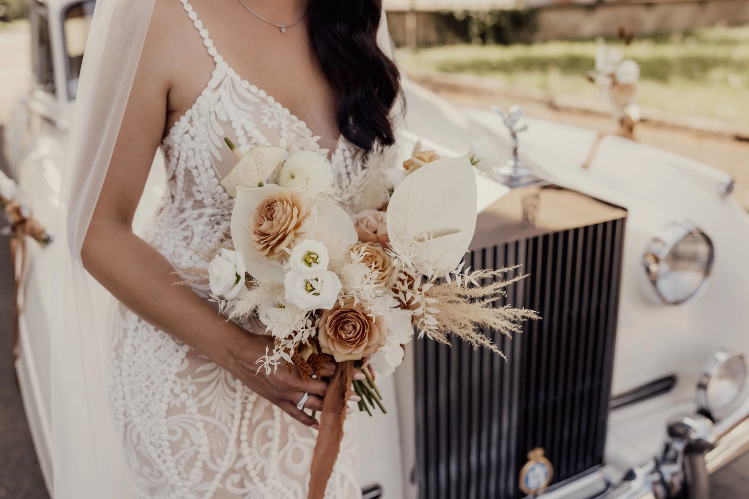 Bride holding bouquet in front of vintage car with lace wedding dress.