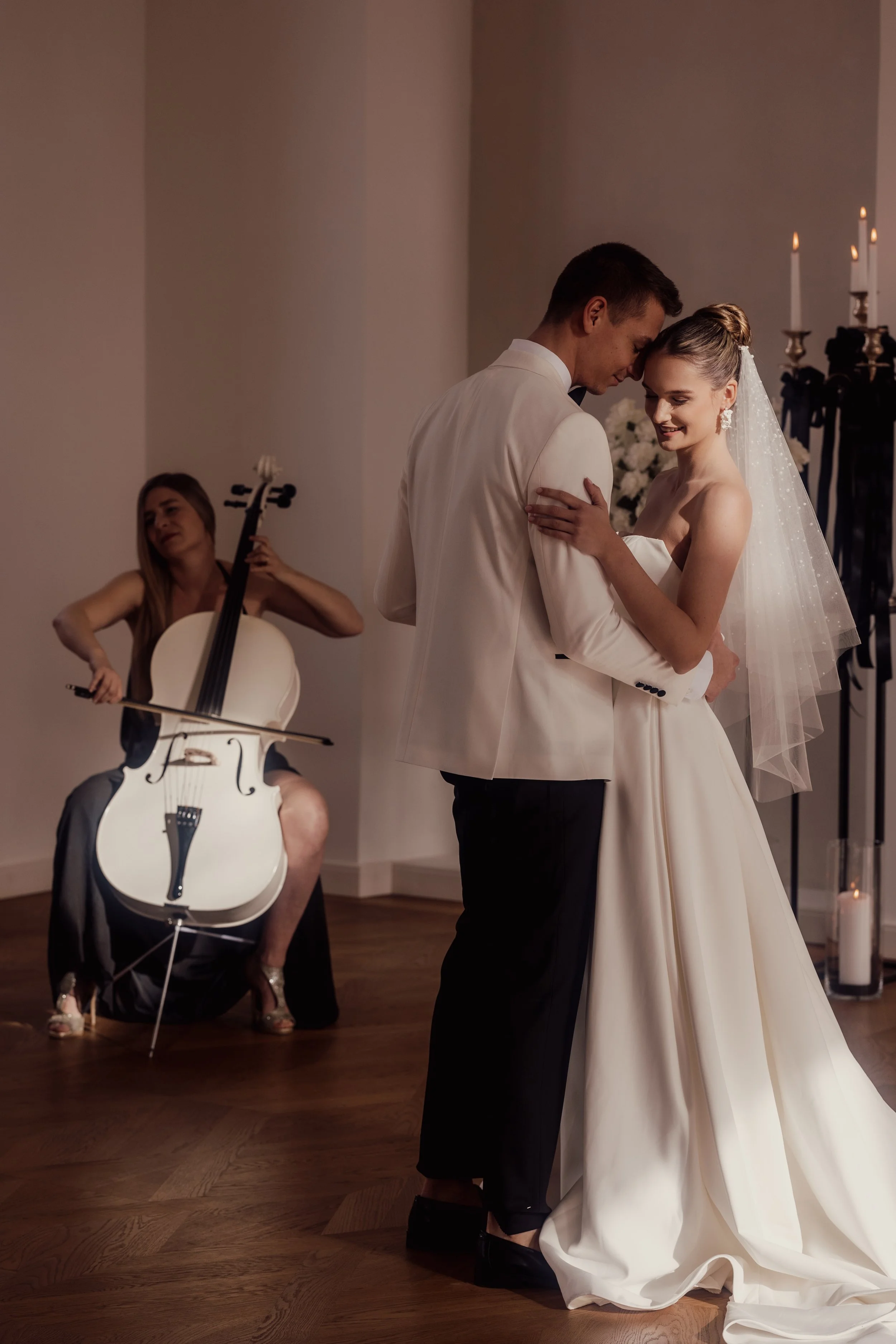 A bride and groom dancing at a wedding, with a cellist playing in the background.