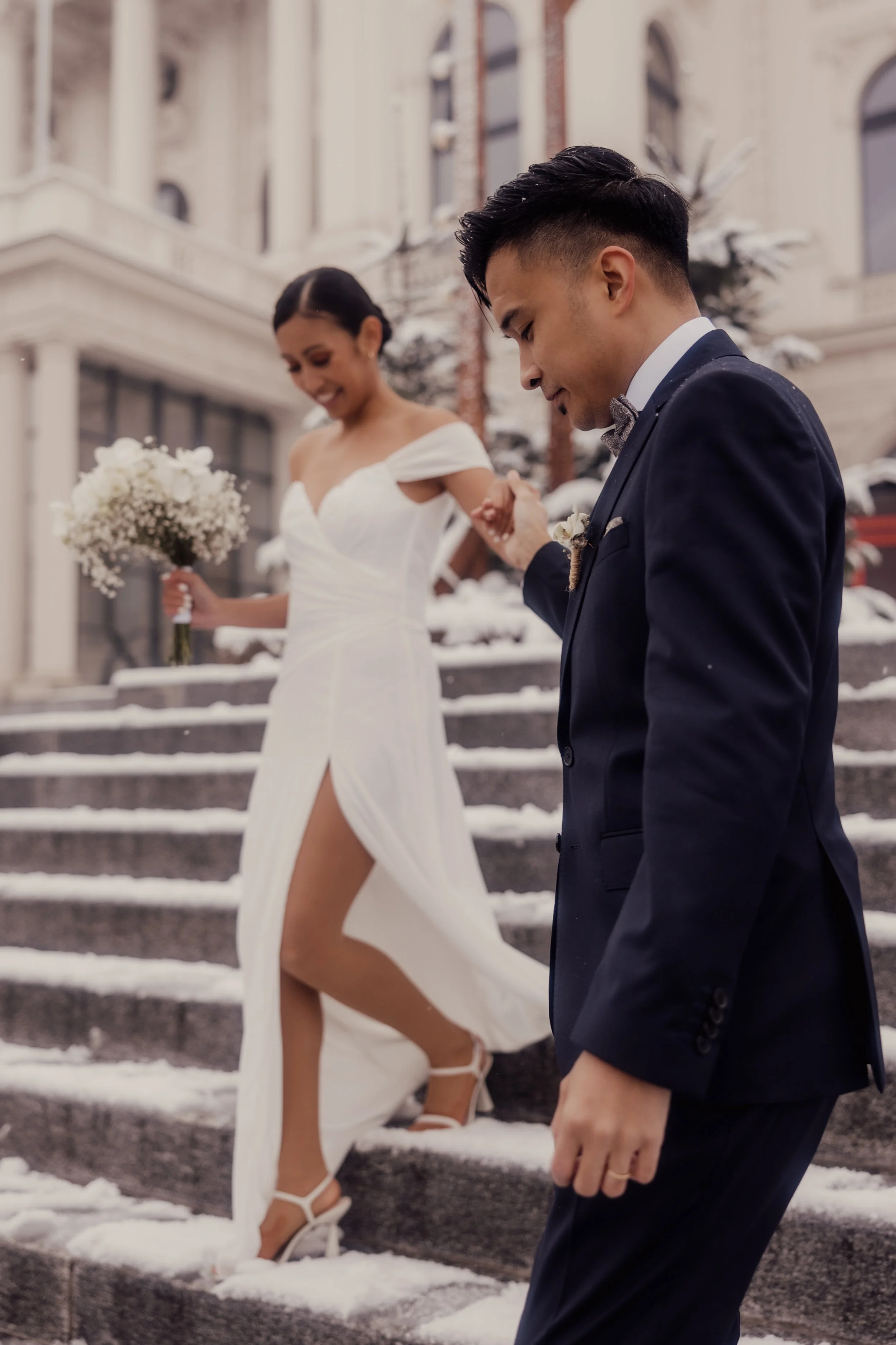 Bride and groom walking down snowy steps, bride holding bouquet