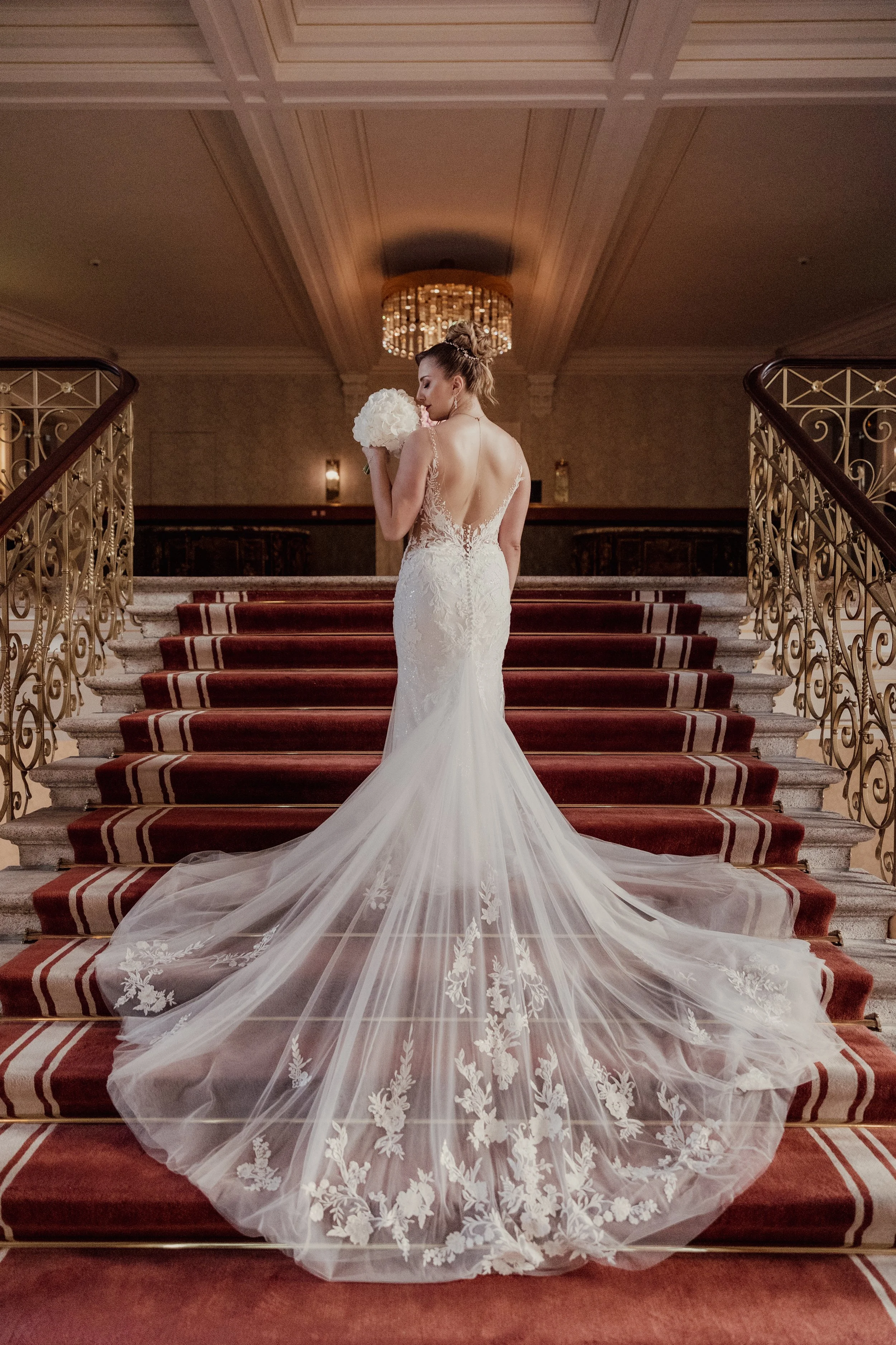 Bride on staircase with elegant lace wedding dress and bouquet