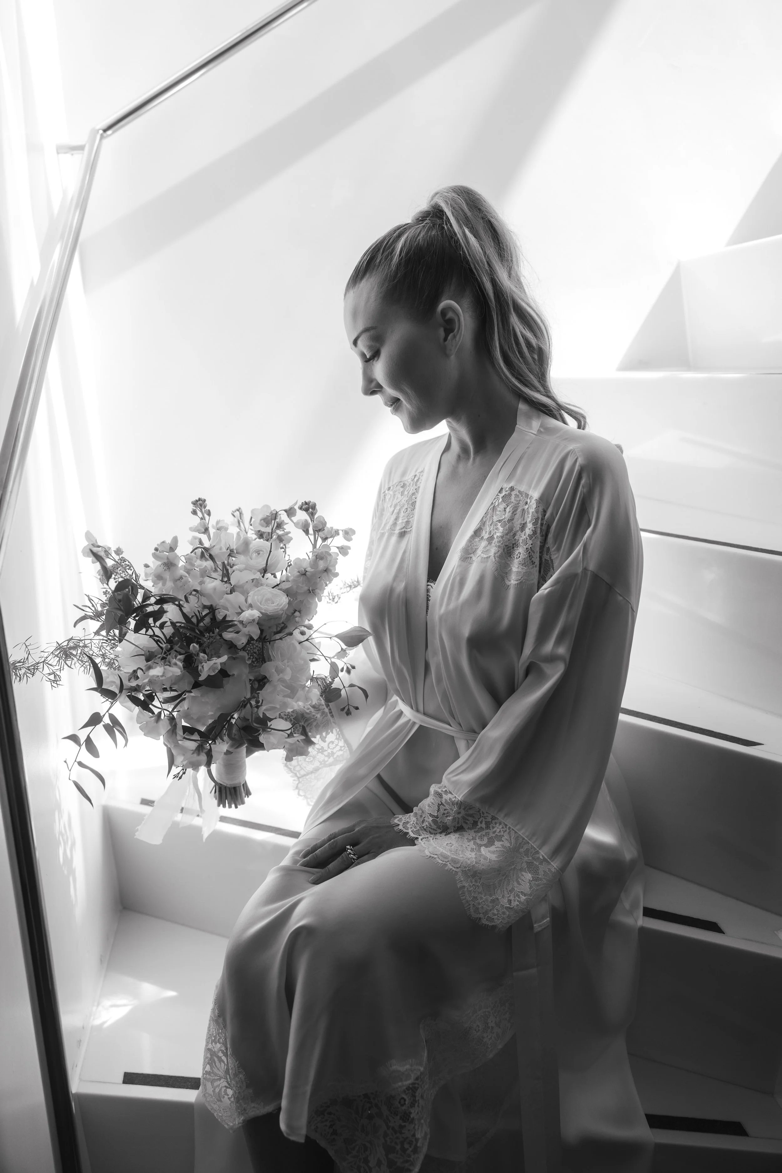 Woman in satin robe holding a bouquet on stairs, black and white photo.