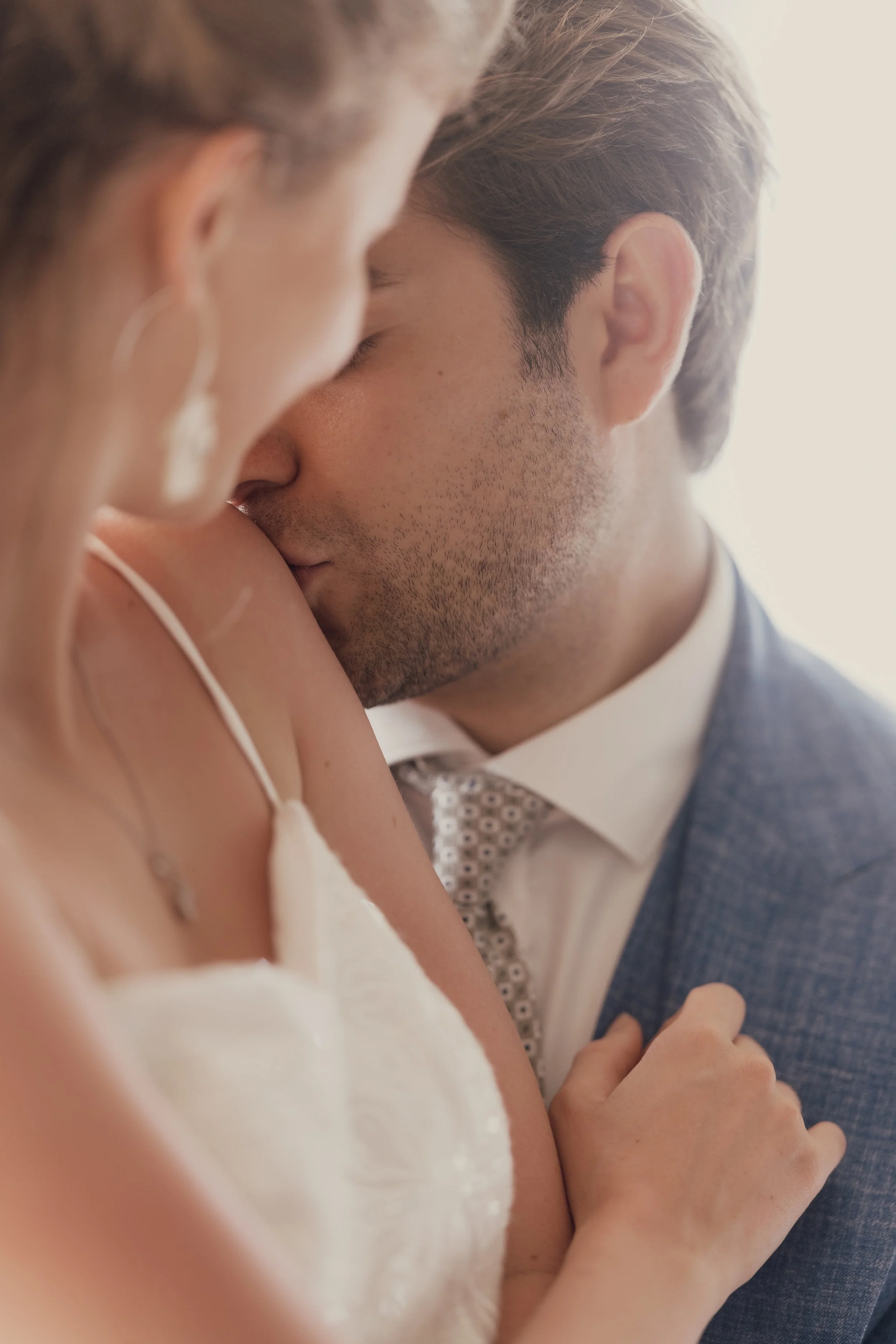 Close-up of a couple in formal attire, with the man gently kissing the woman's shoulder.