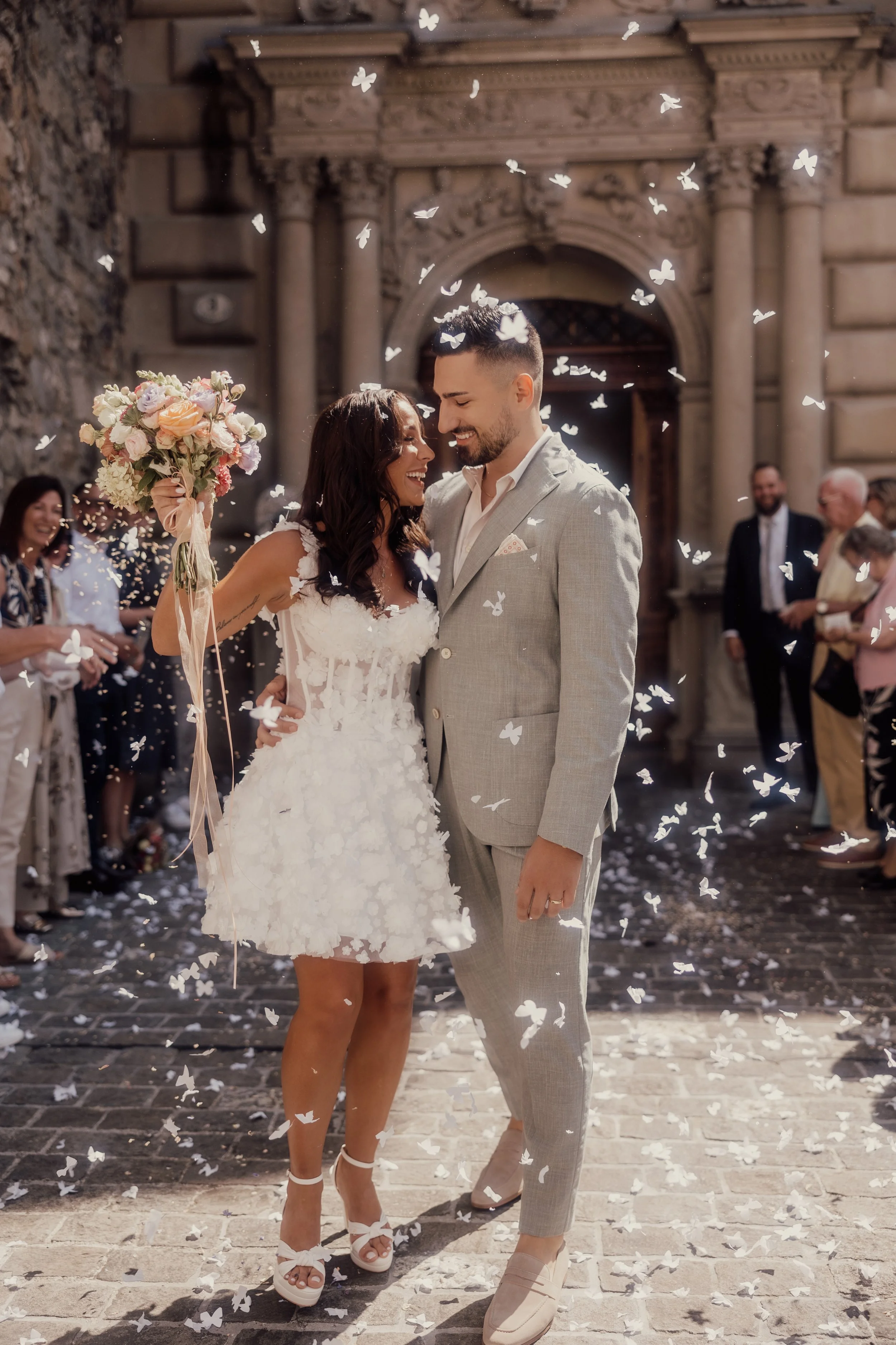 Bride and groom surrounded by confetti outside a building.