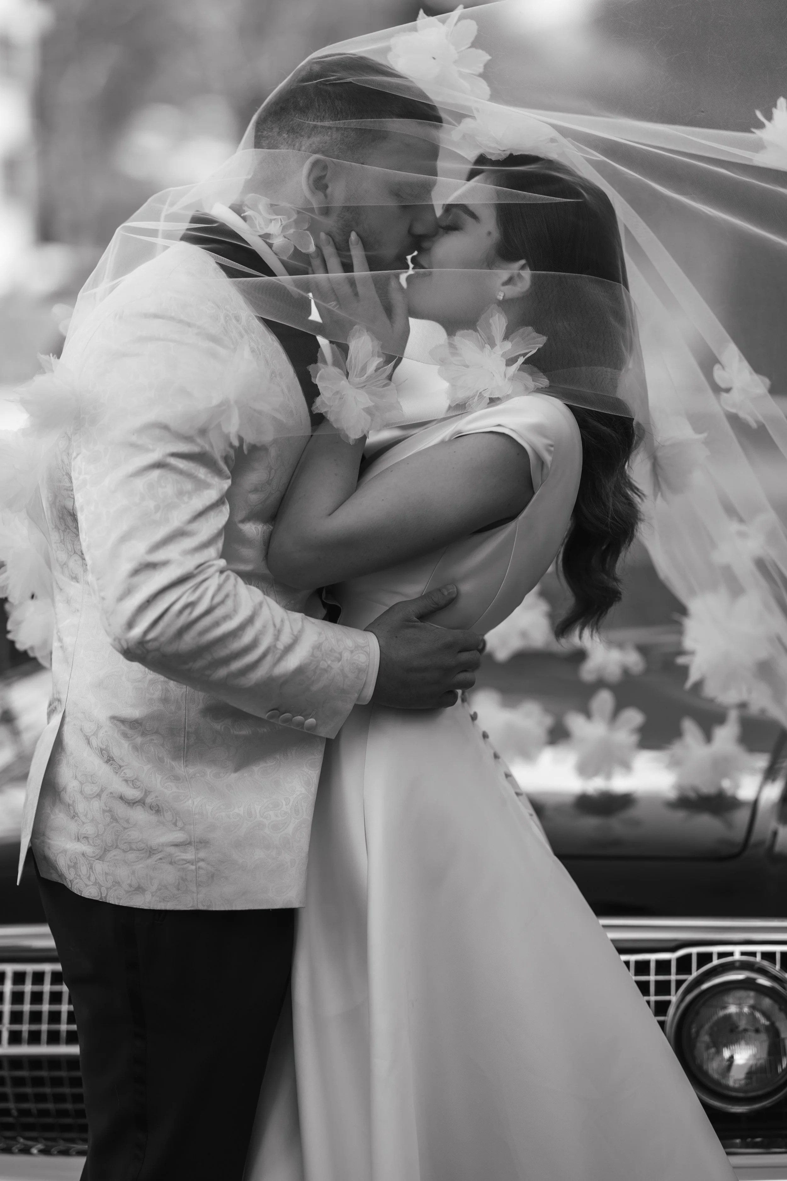 Bride and groom kissing under a veil in black and white