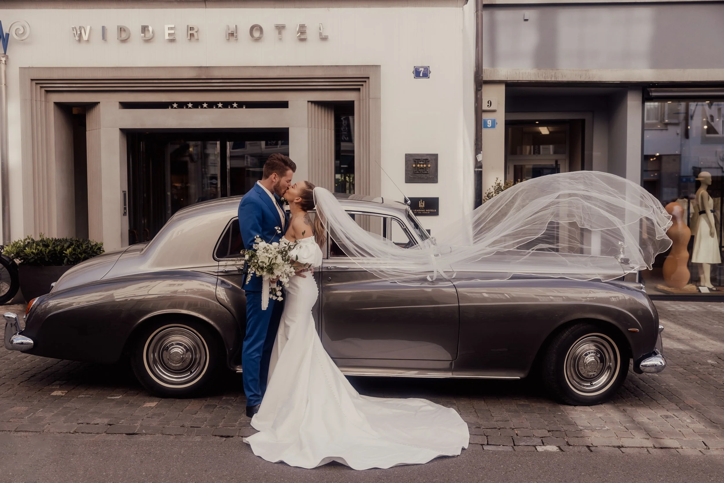 Bride and groom kissing by a classic car in front of Widder Hotel.