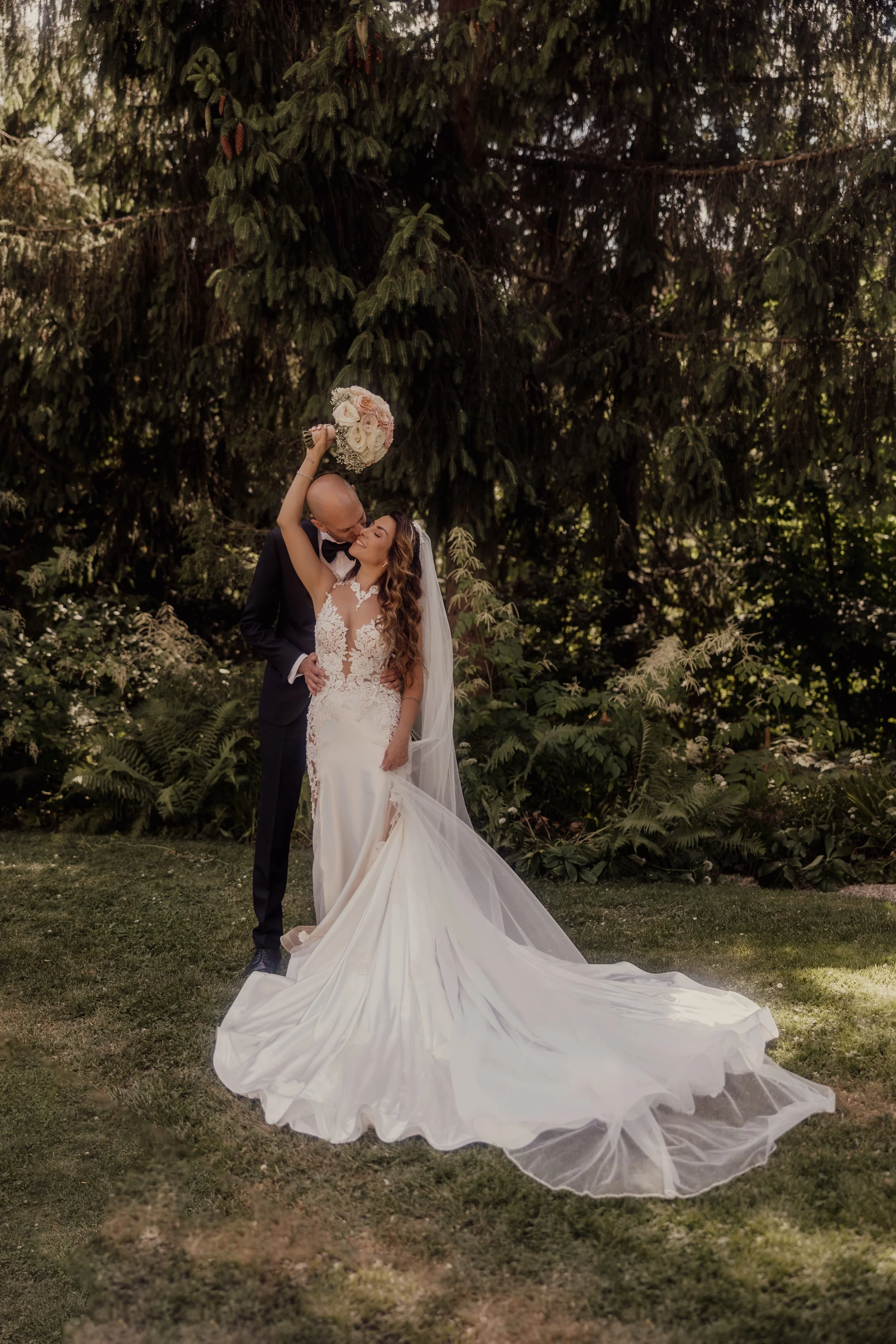 Bride and groom kissing in a garden with a bridal dress and bouquet.