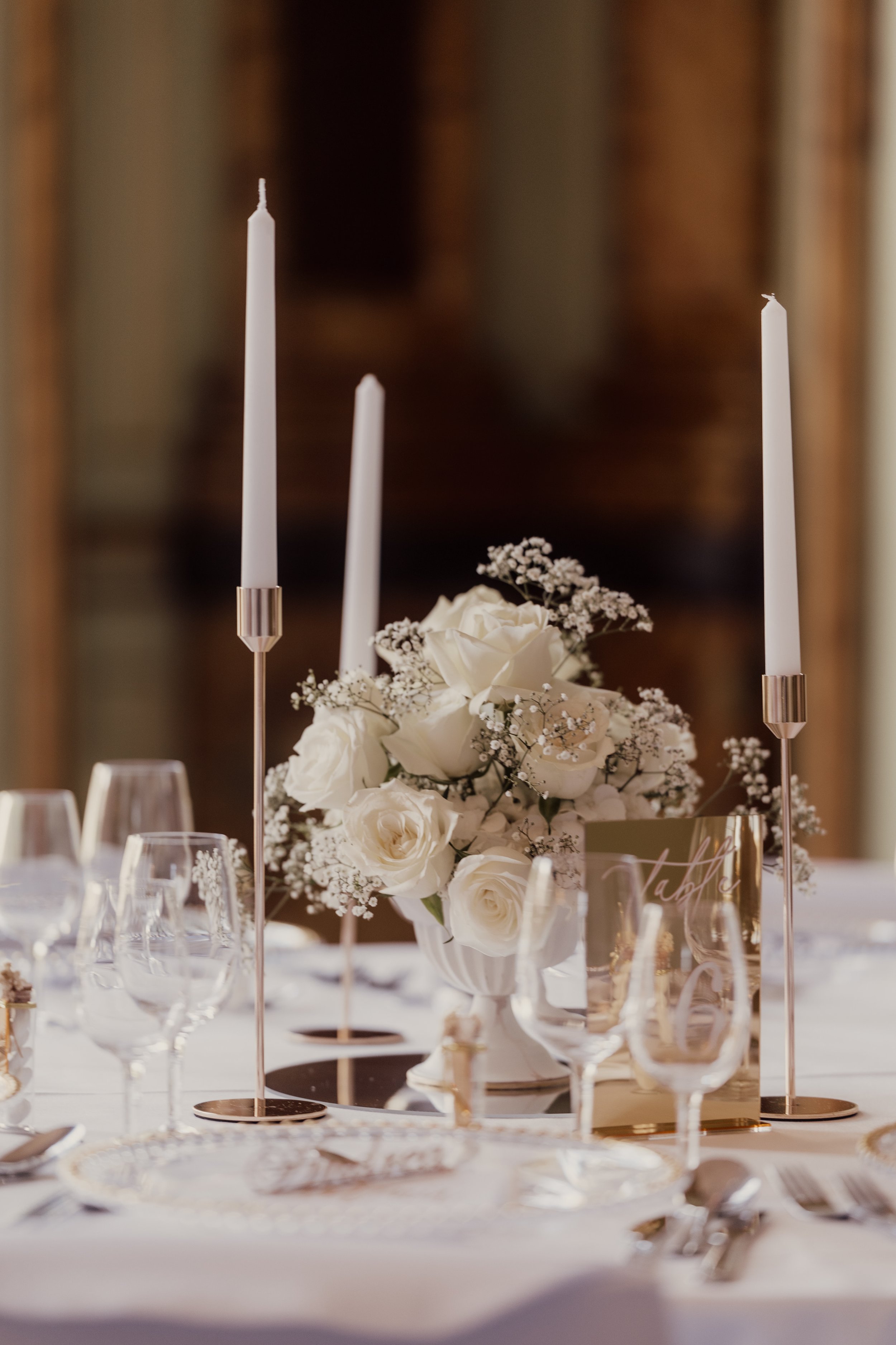 Elegant table setting with tall white candles, a bouquet of white roses and baby's breath, glassware, and tableware.