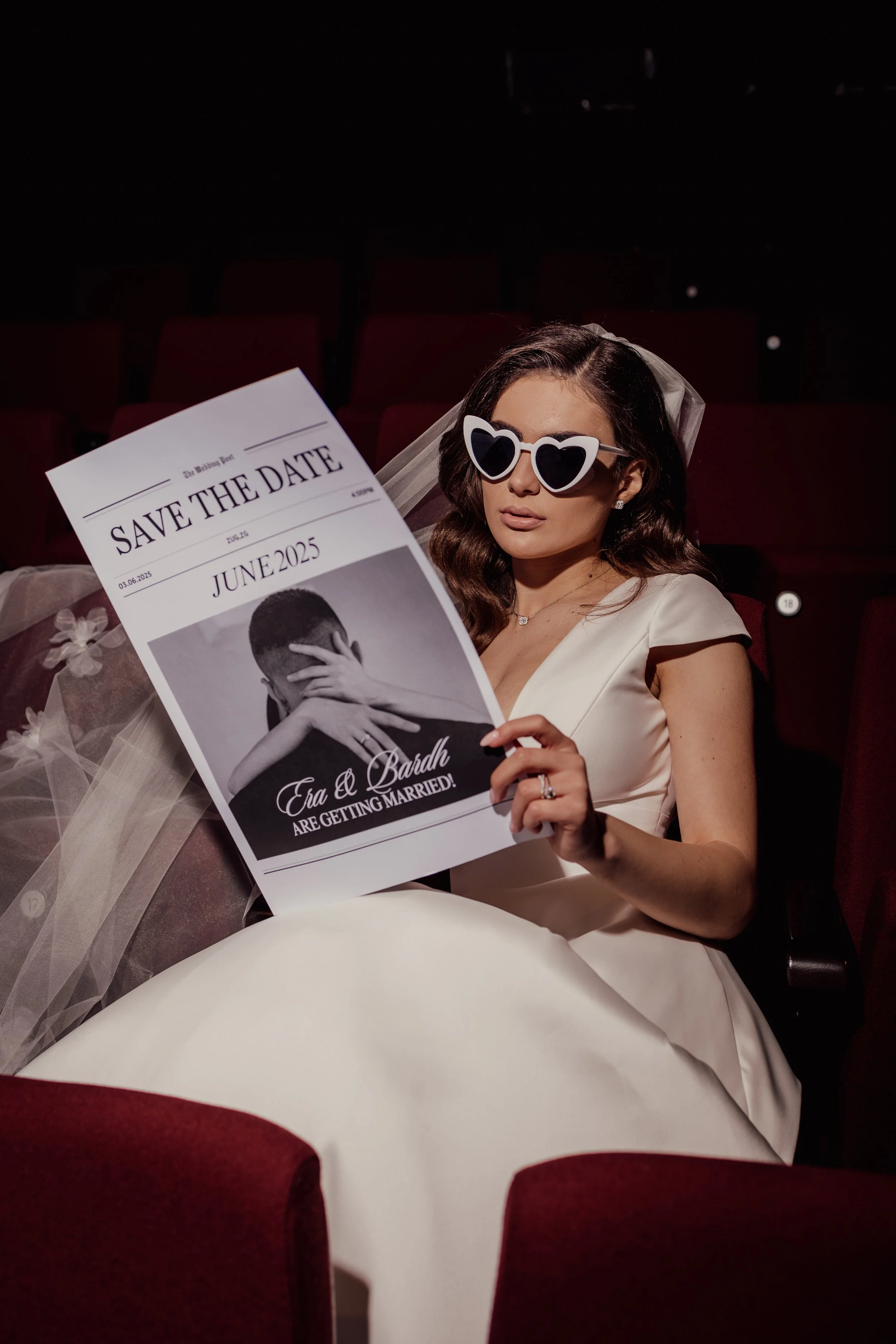 Bride wearing heart-shaped sunglasses holding a black and white wedding save-the-date card.