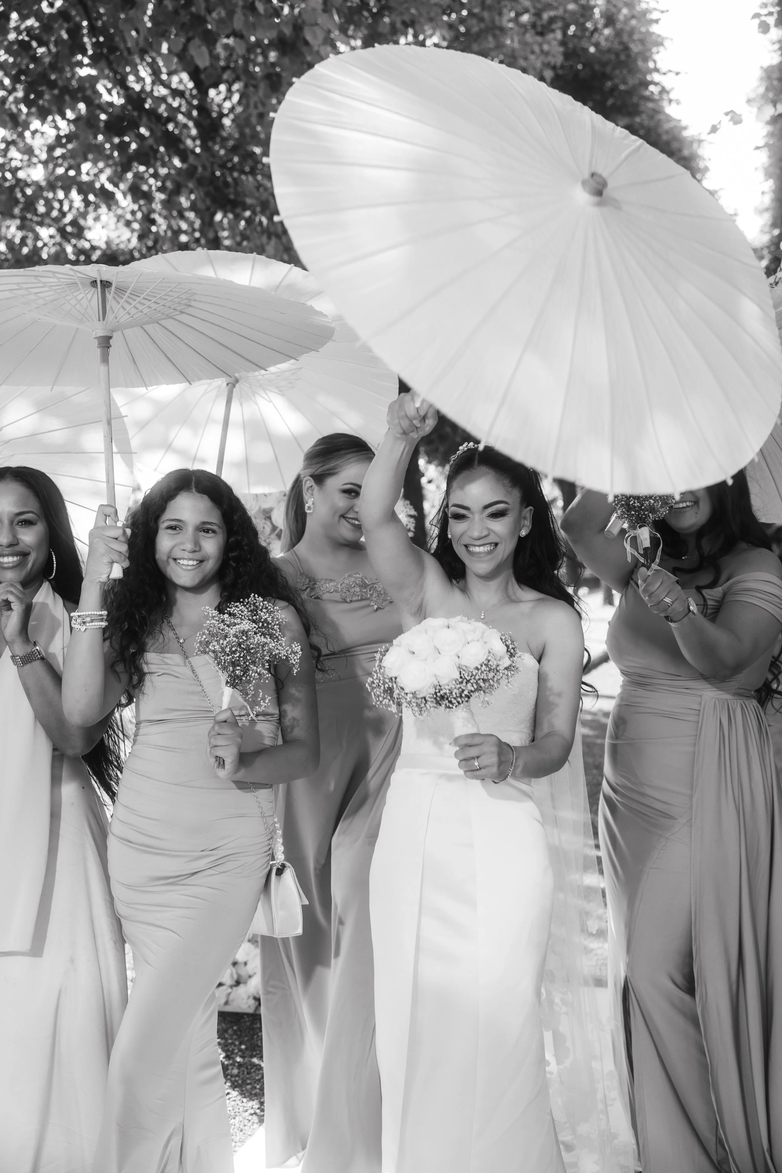 Bridal party posing outdoors with parasols and bouquets, black and white photo.