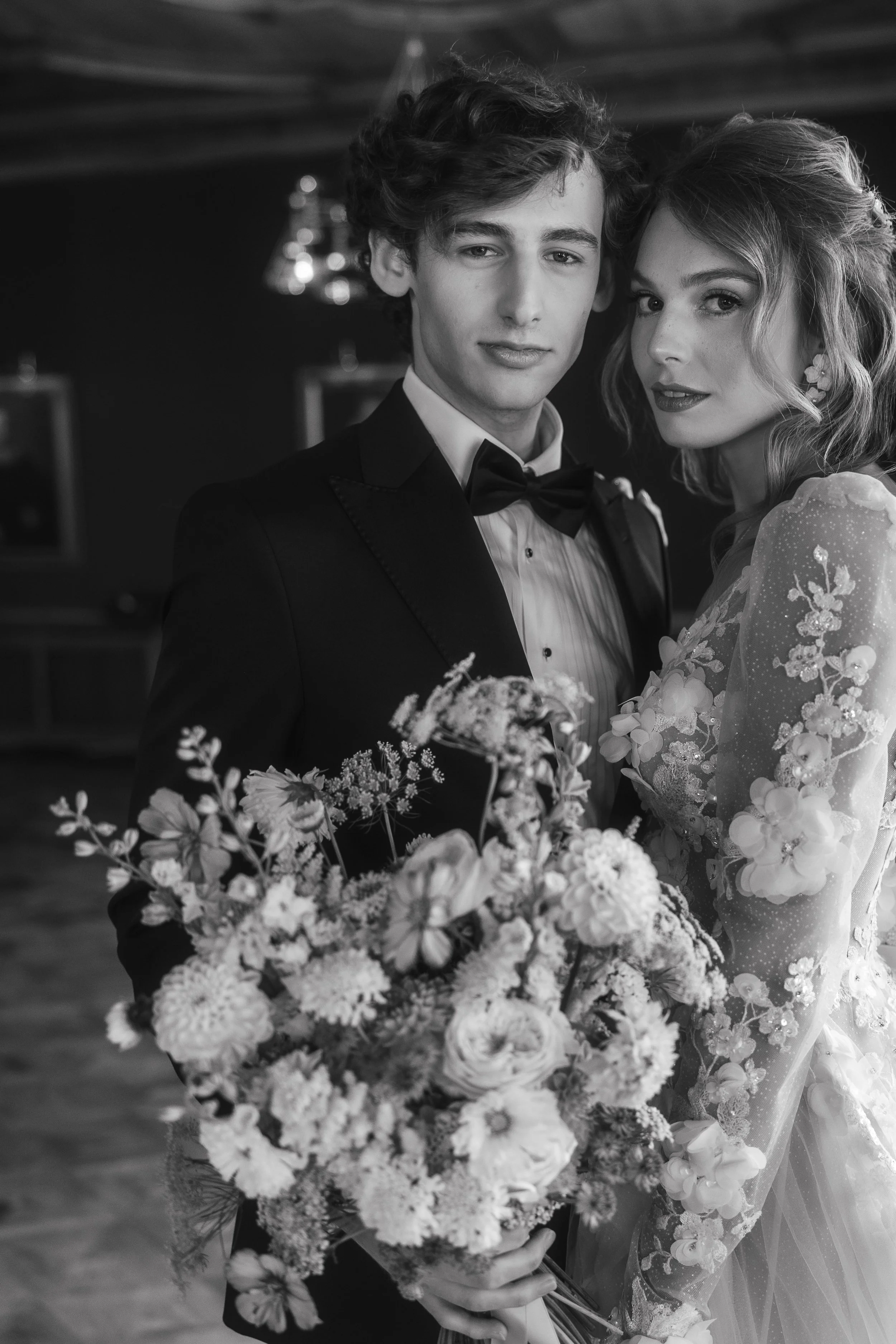 Black and white photo of a couple in formal attire with a large bouquet of flowers.