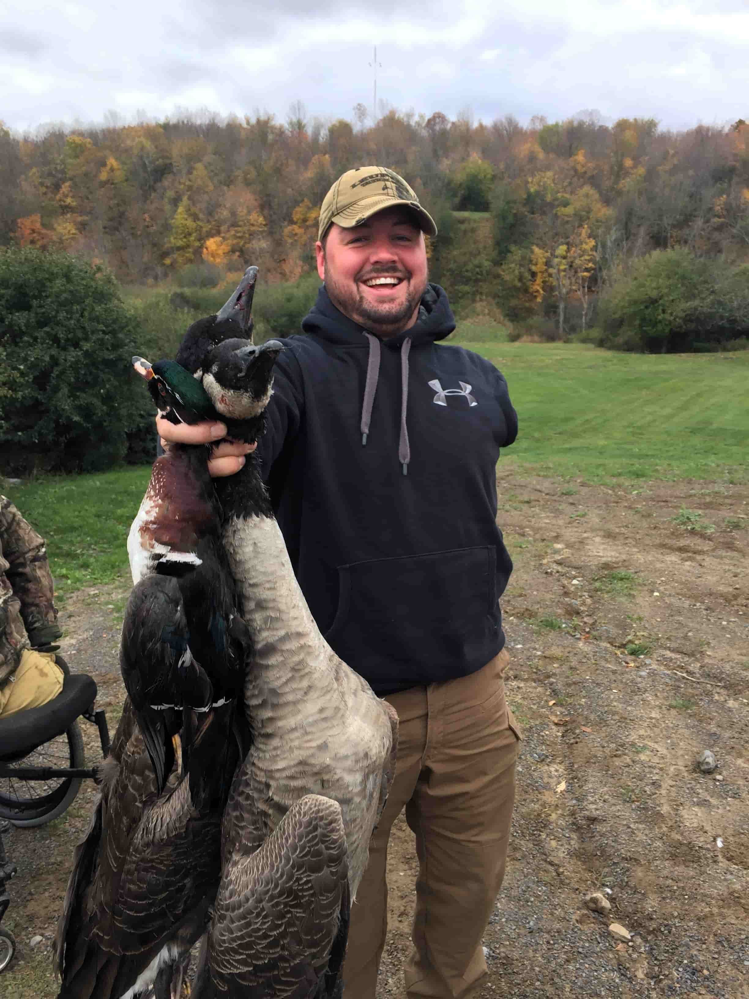 Wounded veteran participating in an NPLB Outdoors waterfowl hunt, smiling and holding harvested geese during an adaptive outdoor experience.