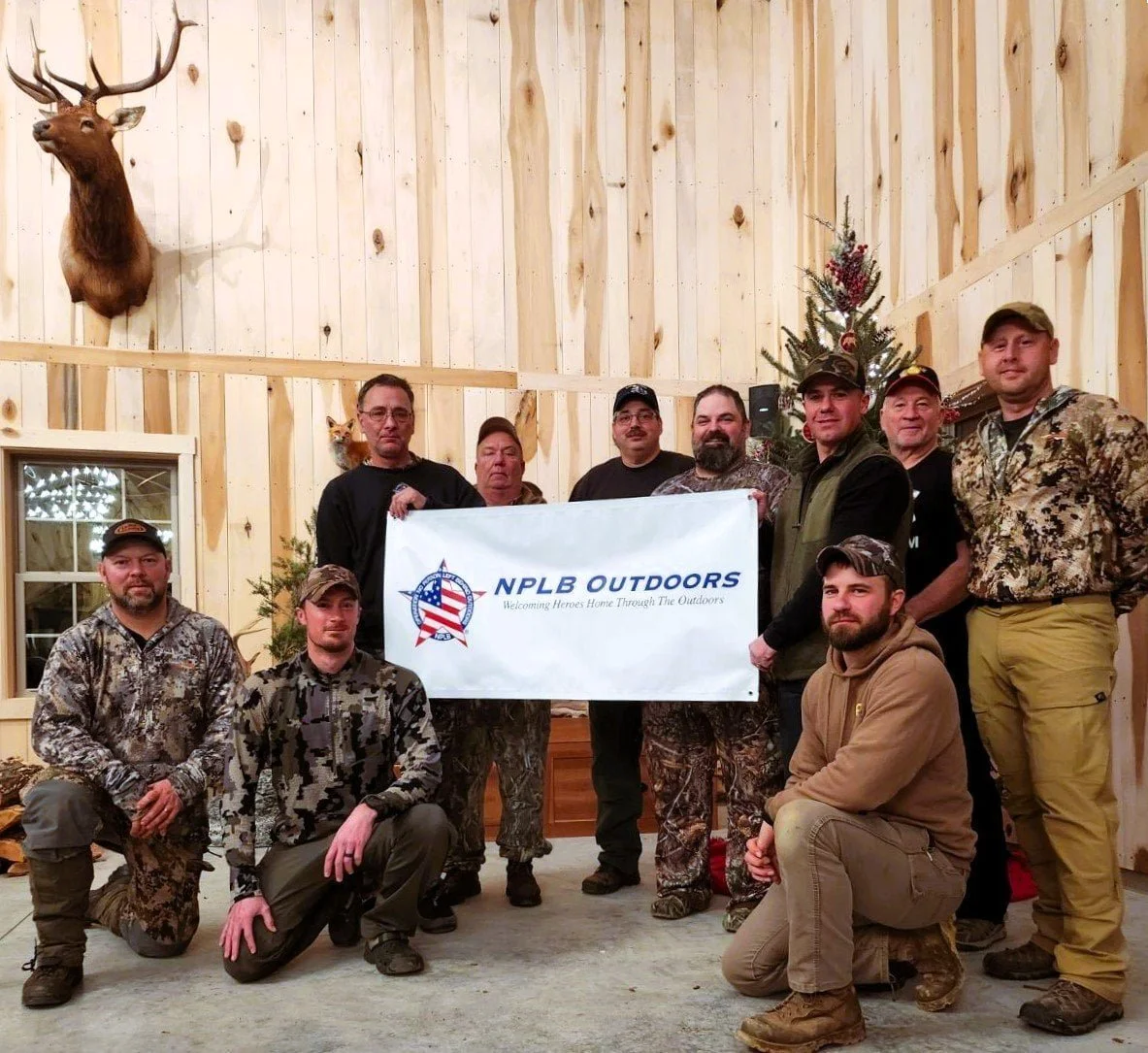 Veterans and volunteers at an NPLB Outdoors Indiana deer hunt, posing with the NPLB Outdoors banner during an adaptive hunting event.