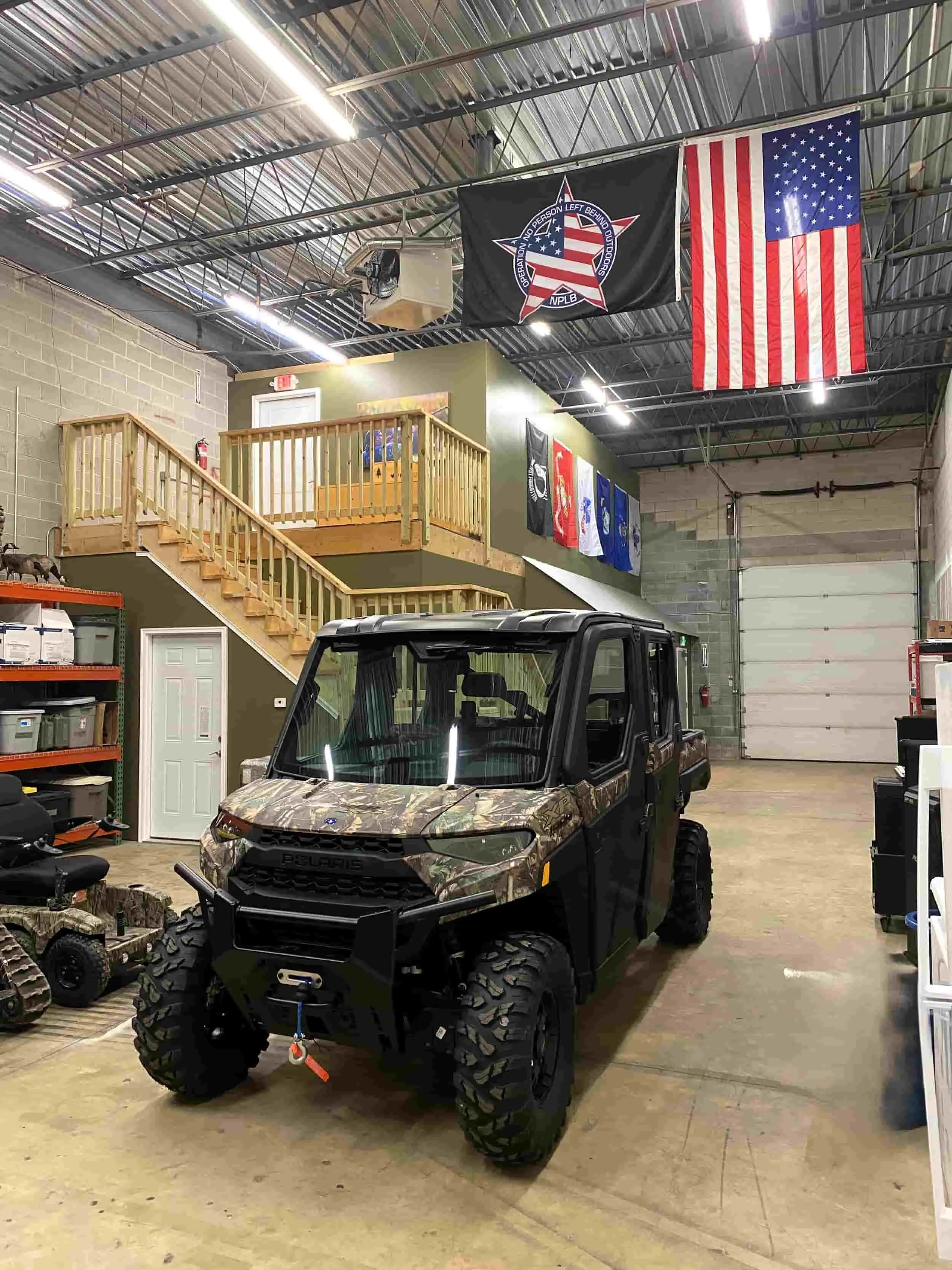 Inside the NPLB Outdoors headquarters showing adaptive all-terrain vehicles, American and military branch flags, and equipment used for veteran outdoor programs.