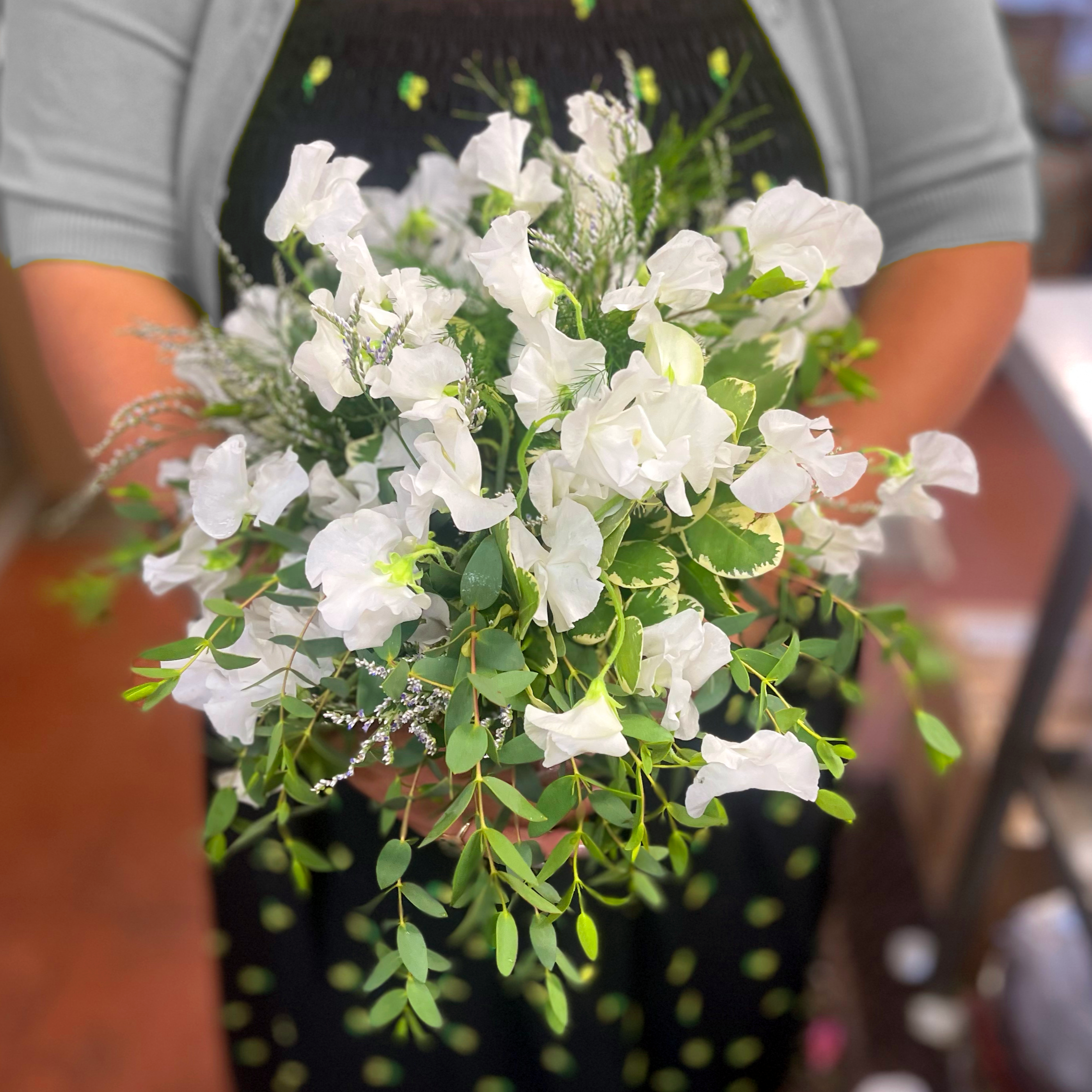 A person holding a bouquet of white and green flowers and foliage, with the person's gray-sleeved arms visible.