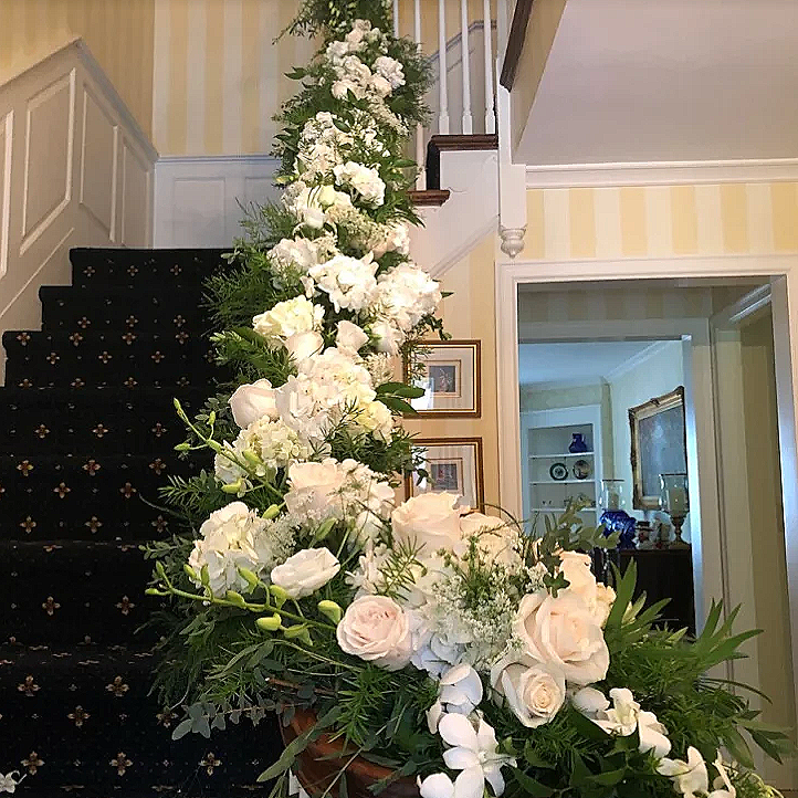 Floral arrangement of white roses and greenery on a staircase railing in a home interior.