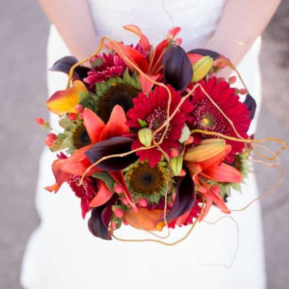 Bride holding a bouquet of colorful flowers including red and orange lilies, dark purple calla lilies, and gerbera daisies.
