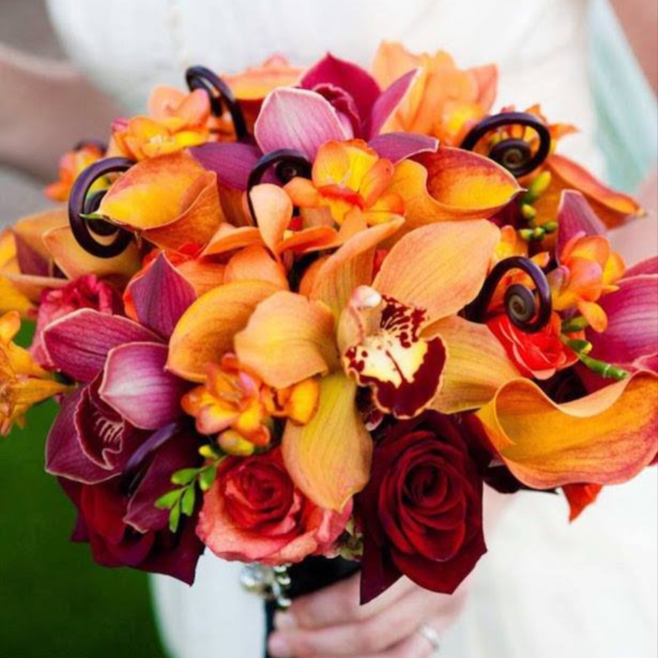 A vibrant bouquet of assorted flowers including roses, orchids, and other colorful blossoms, held by a person.