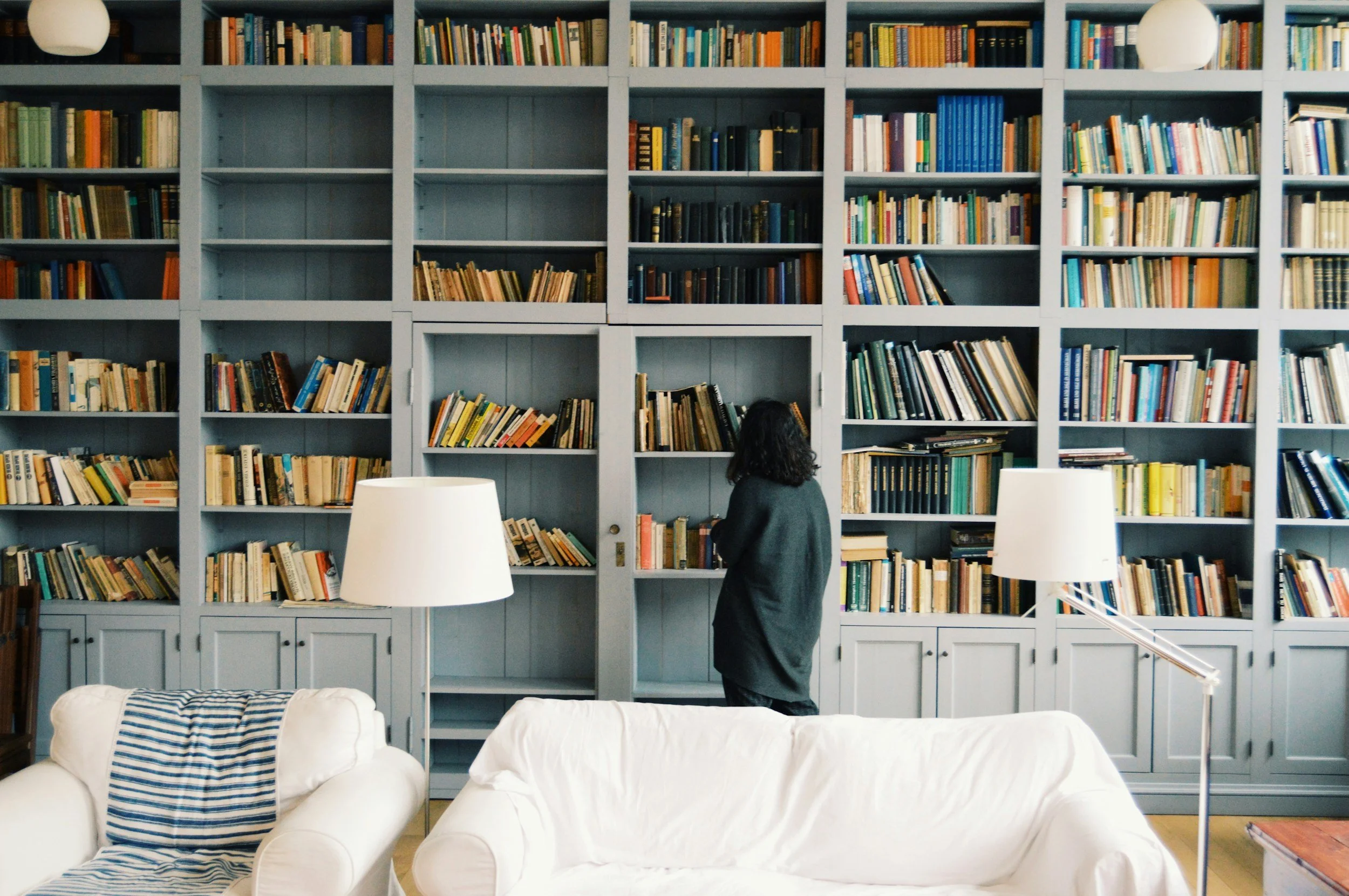 Full wall bookshelf with woman exploring the book titles.