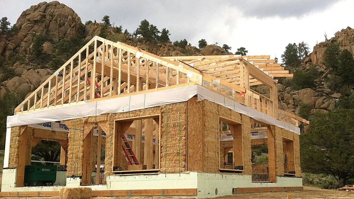 Straw bale house under construction with roof being framed.