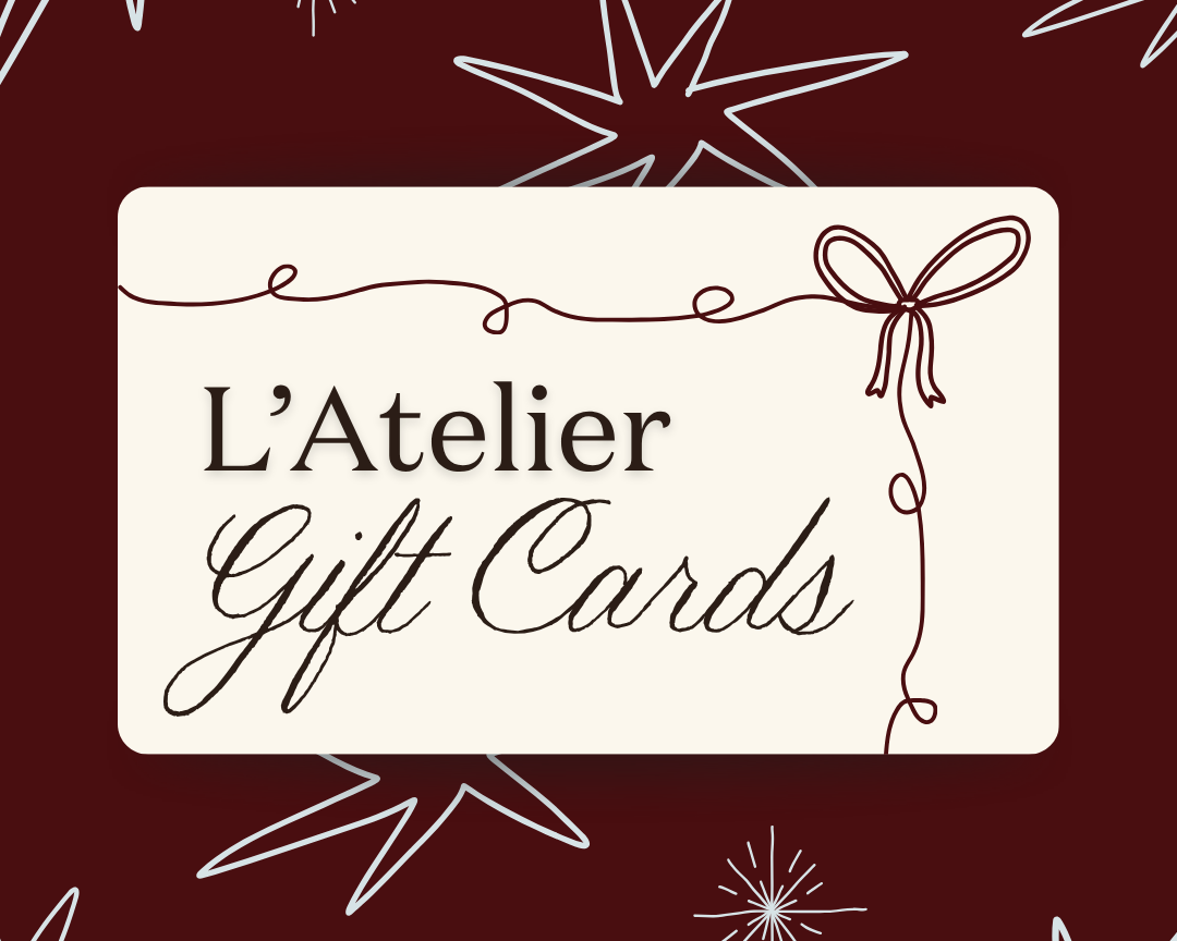 A graphic with a dark red background featuring white and brown starburst and snowflake designs. In the center, a white rectangular label reads "L'Atelier Gift Cards" with decorative brown lines and a bow illustration.