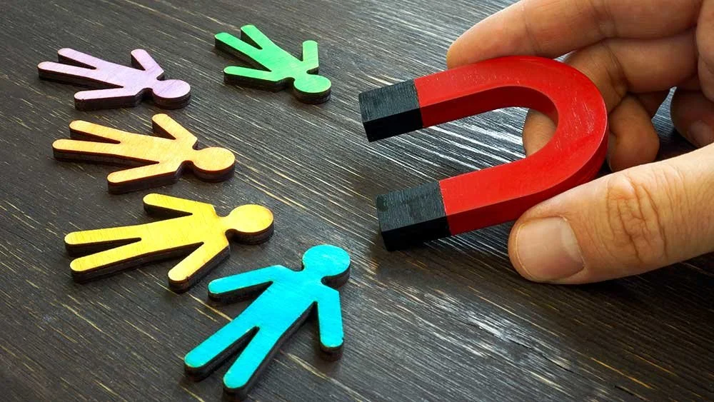 A diverse group of smiling professionals sitting at a long table in a modern office, with sunlight streaming in through windows.