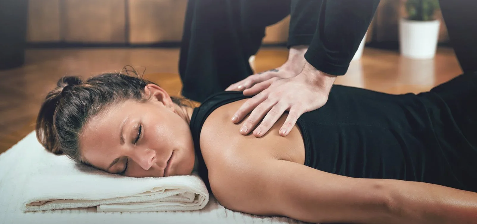 Woman lying face down on a massage table receiving a back massage from a therapist.