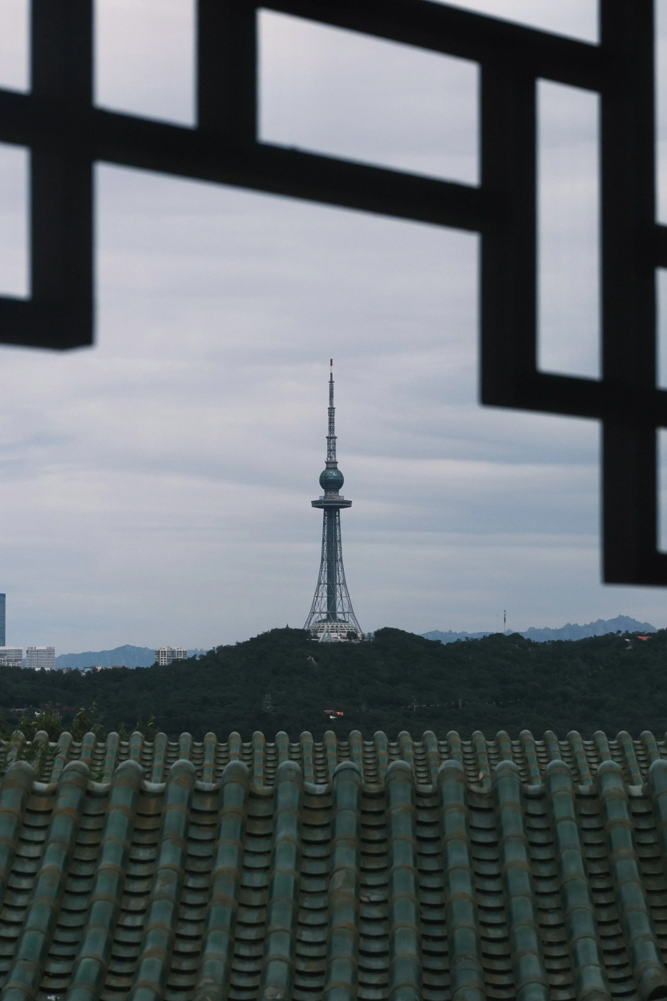 A TV tower on a hill, framed by a window lattice above green roof tiles