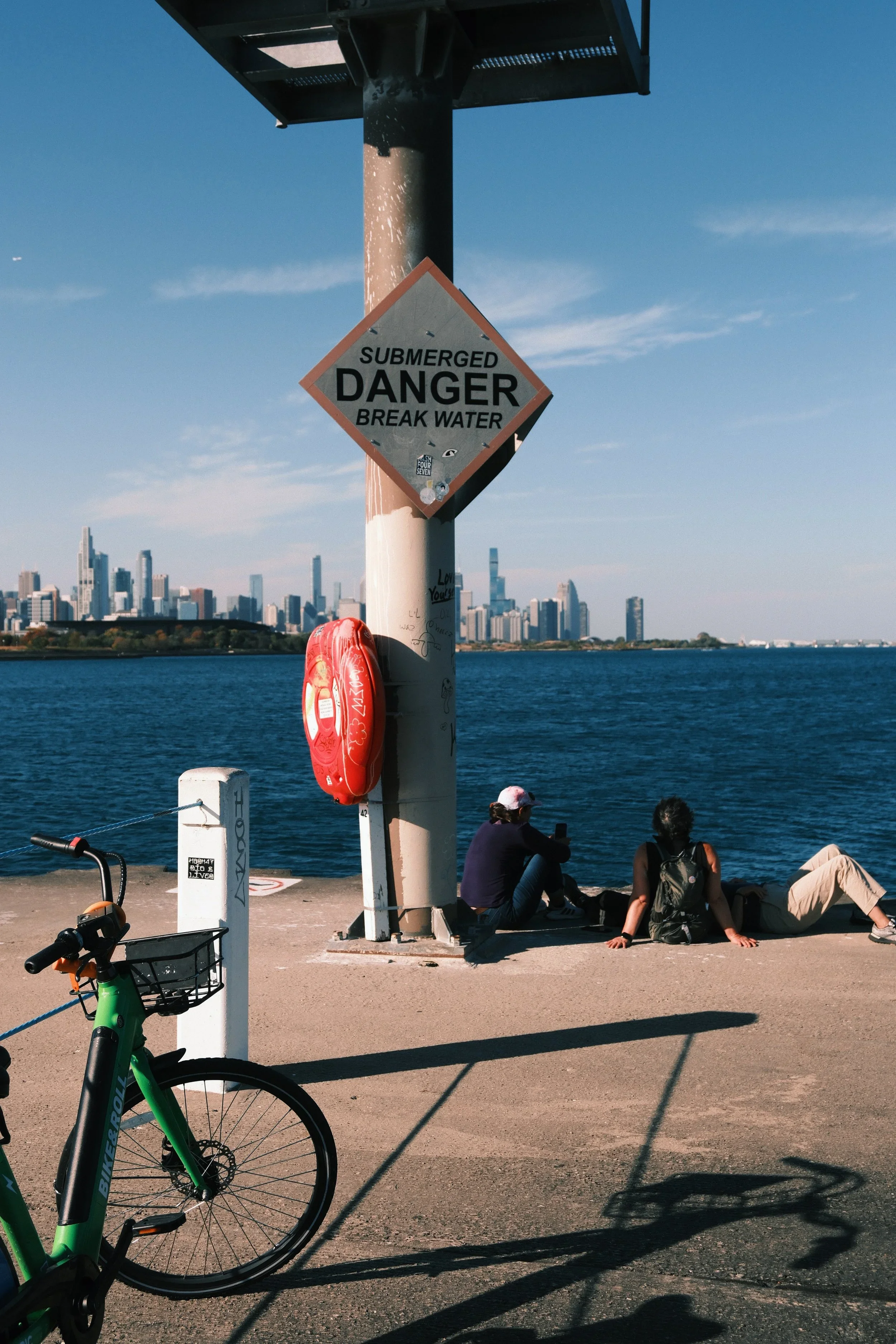 People sitting on the lakefront under a "Danger" sign, a bike in front