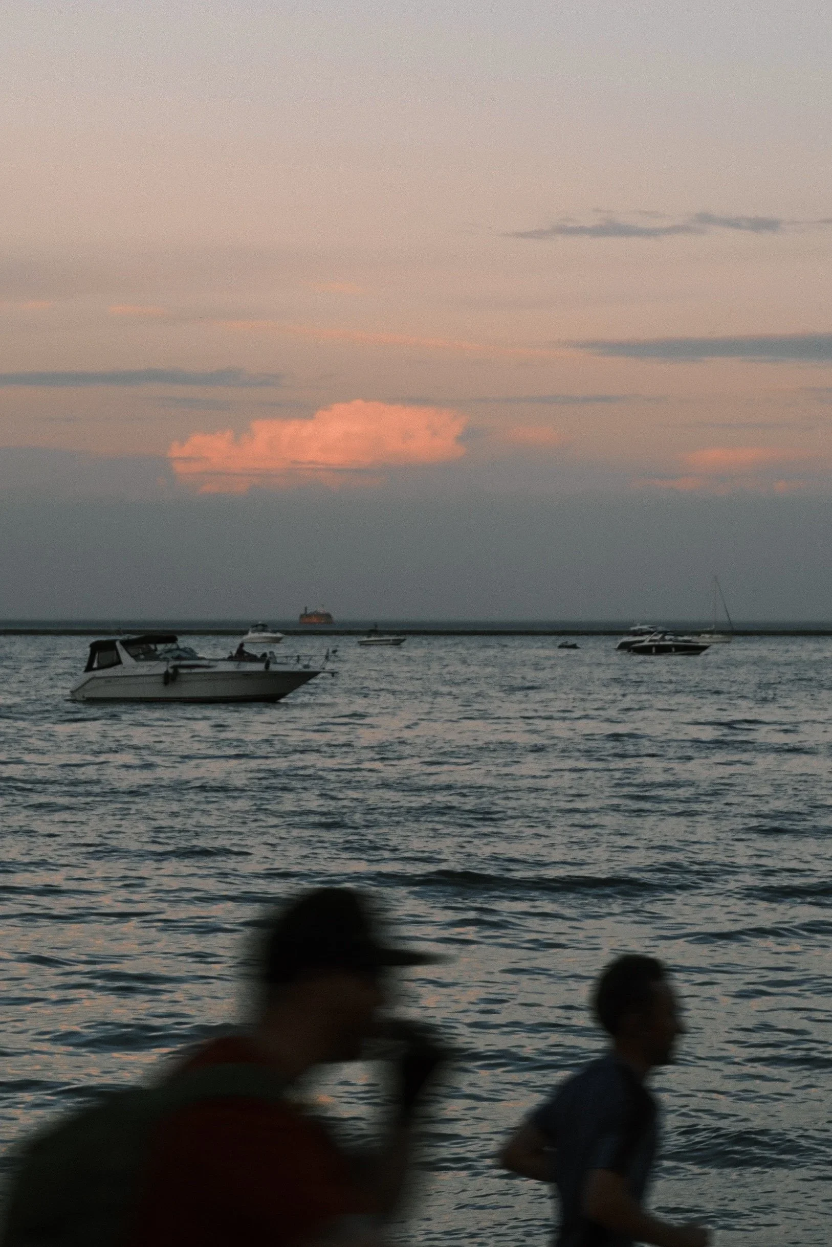 Silhouettes of two people walking past the lake at sunset, boats on the water