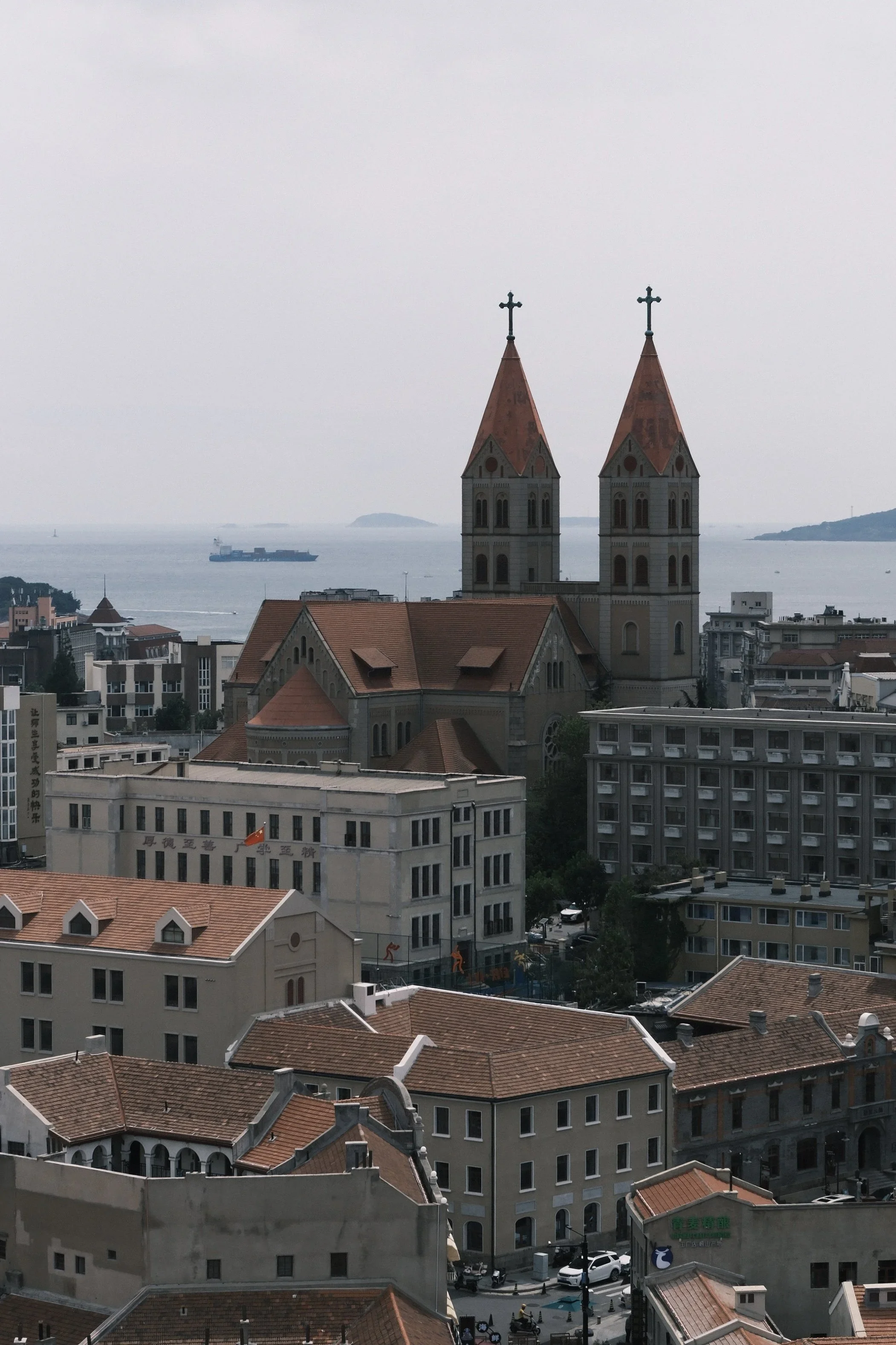 Twin spires of the cathedral rising over red roofs, with the sea behind