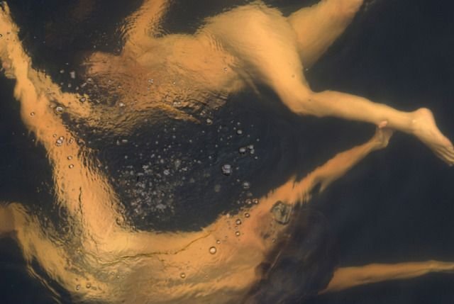 Abstract underwater image of two swimmers, distorted by water surface, with visible bubbles and reflections.