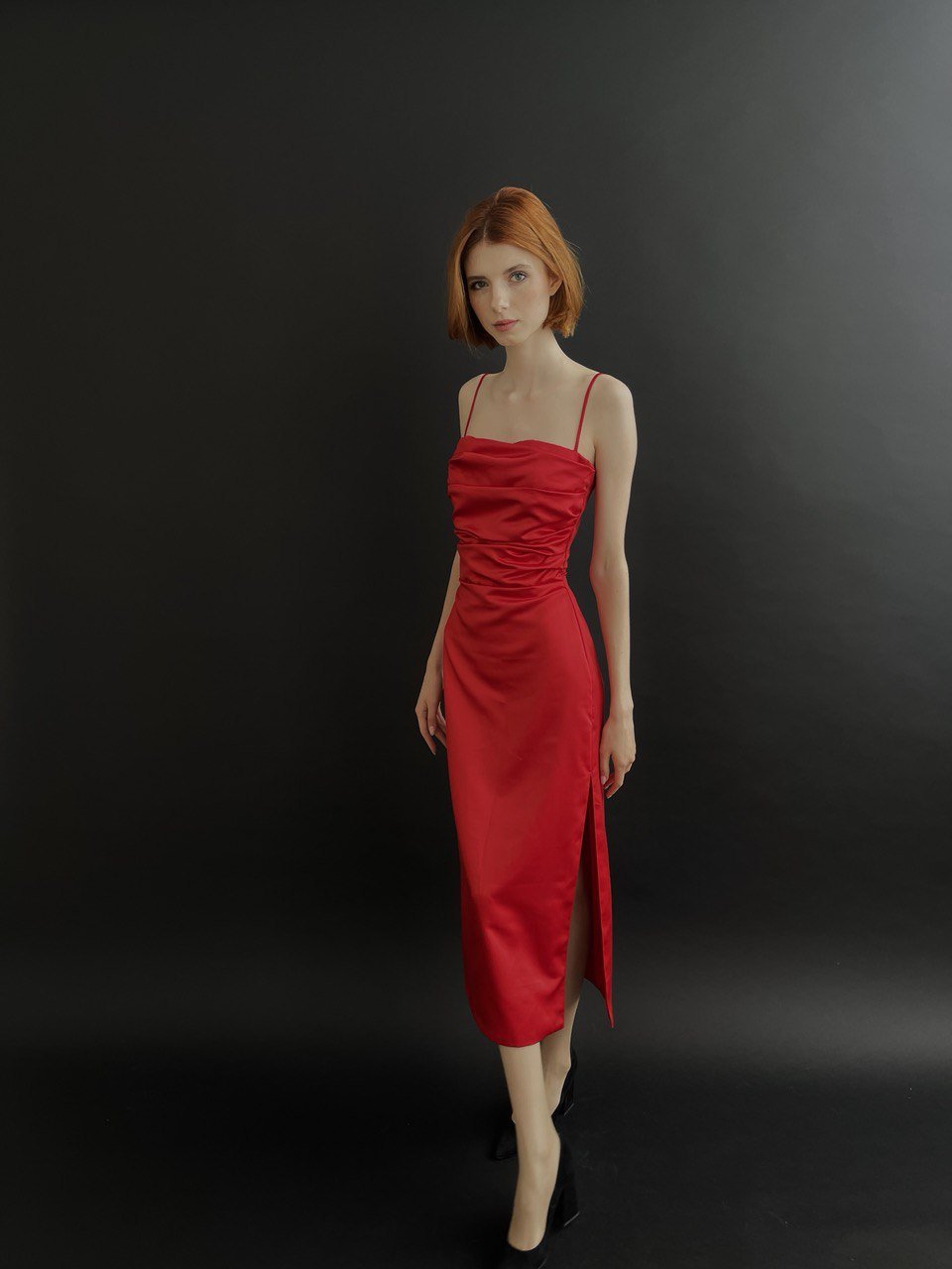 Woman in red dress standing against a dark background. Vast Leaf