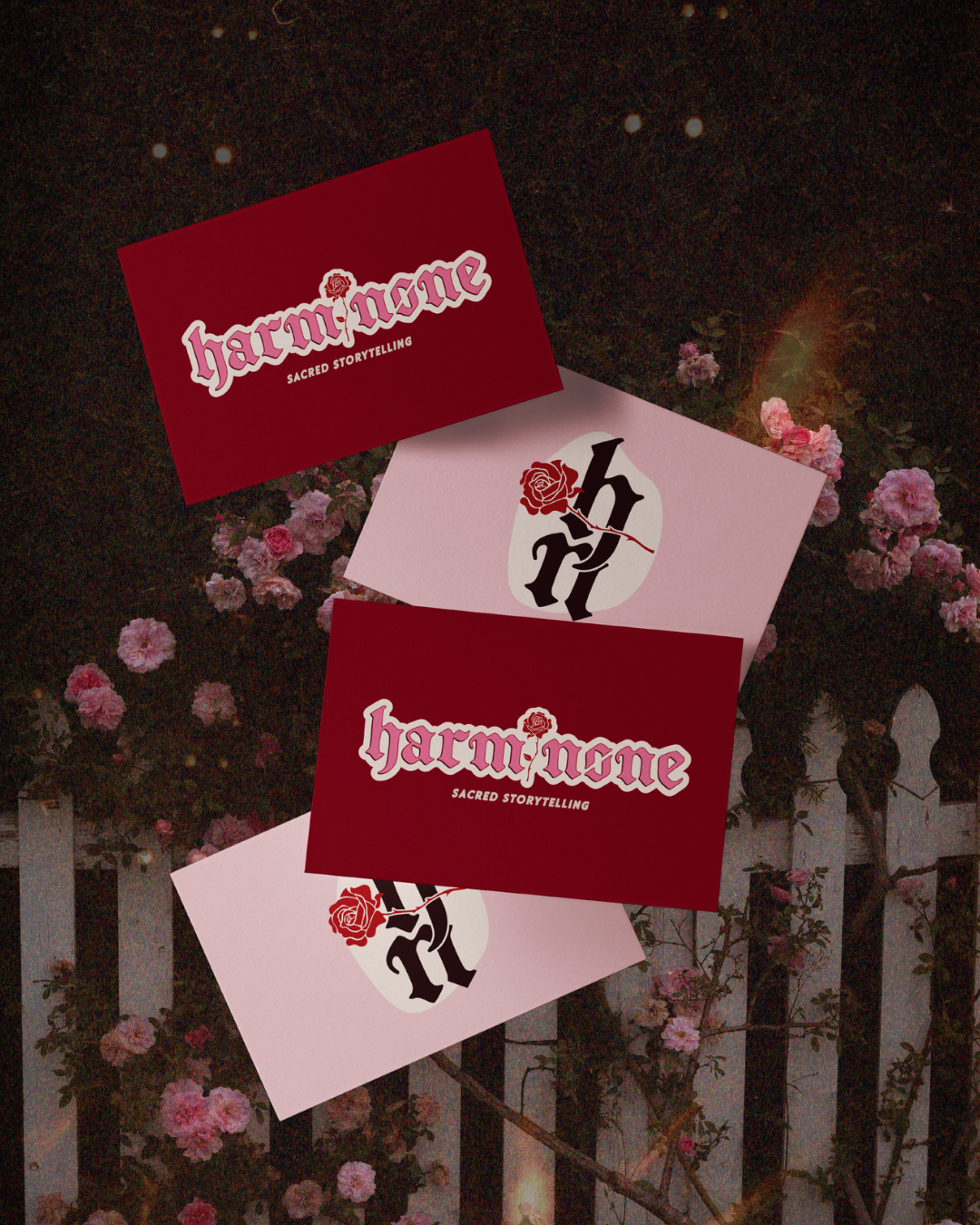 Three business cards with the word 'HarmNone' and a rose logo, laid on pink and red backgrounds, set against a garden with pink flowers and a white fence.