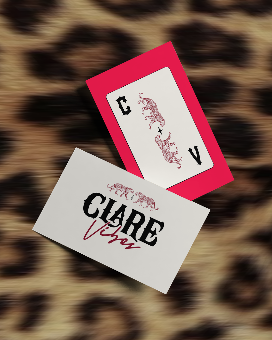 Playing cards on a leopard print surface with a non-standard design of a leopard on the face of the card and the text "Clare Vibe" on the envelope.