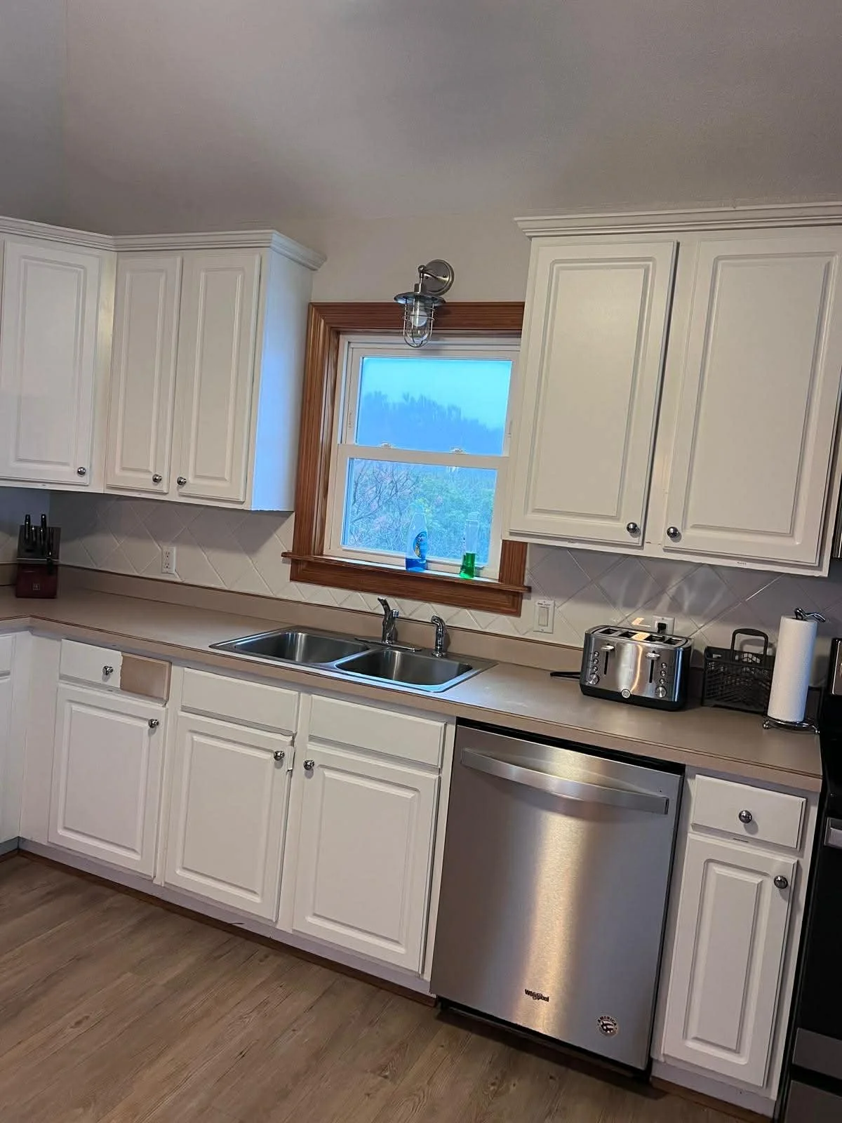 Kitchen with white cabinets, a double sink, window with brown trim, granite countertop, stainless steel mini fridge, toaster, paper towel holder, and a few decorative items on the windowsill.