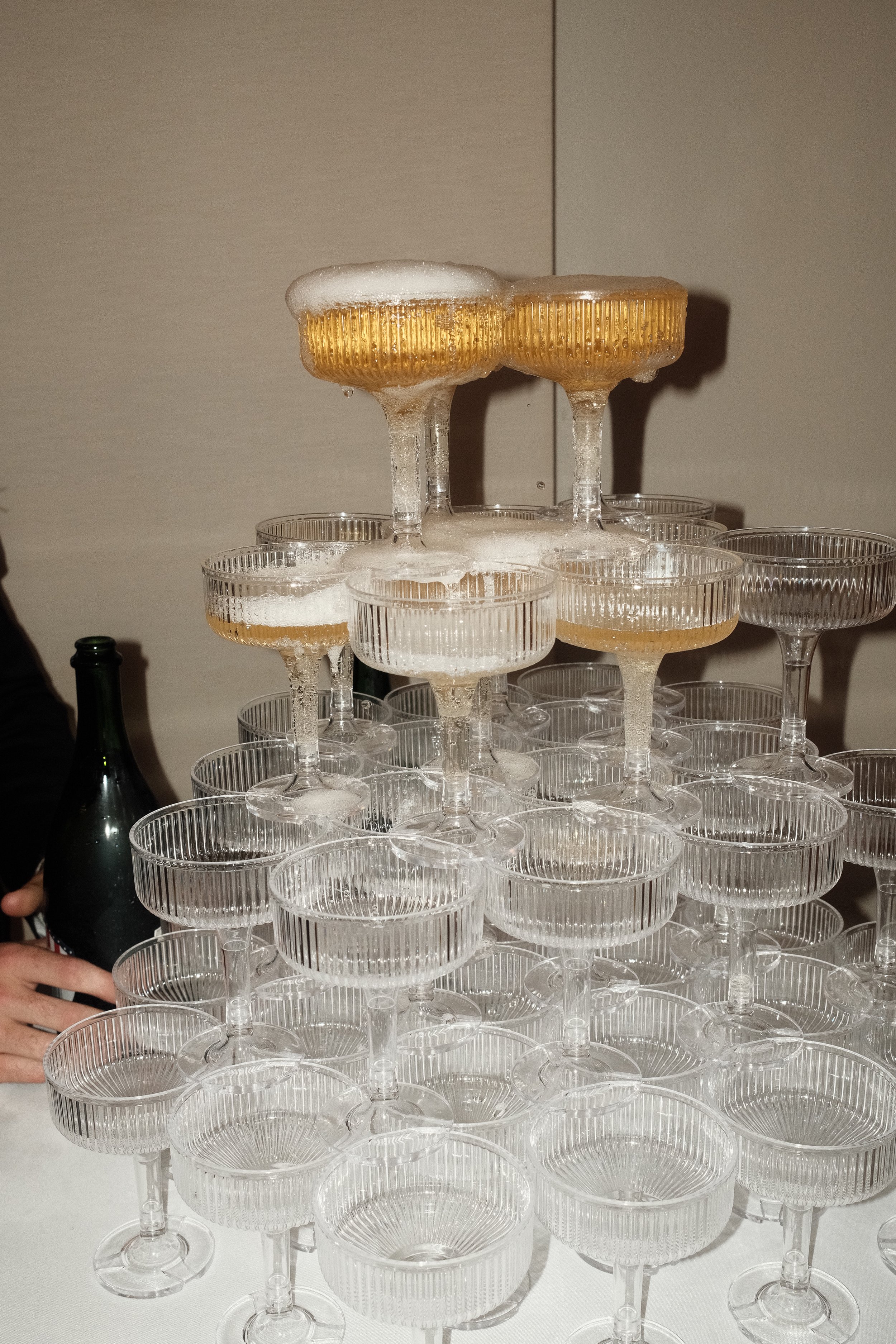 A tower of empty champagne glasses topped with two glasses filled with beer and foam.