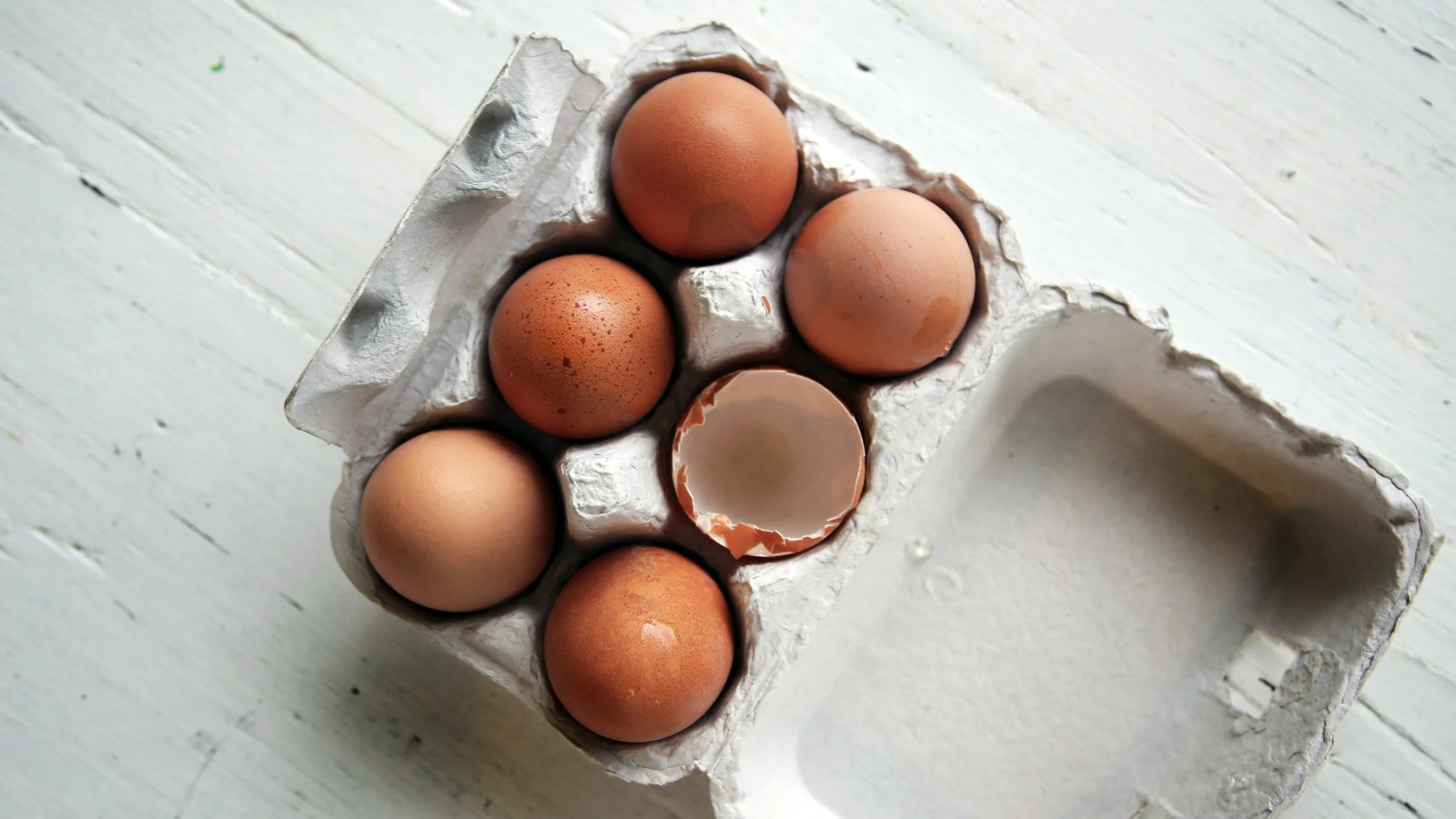 A half carton of eggs, with one egg cracked open