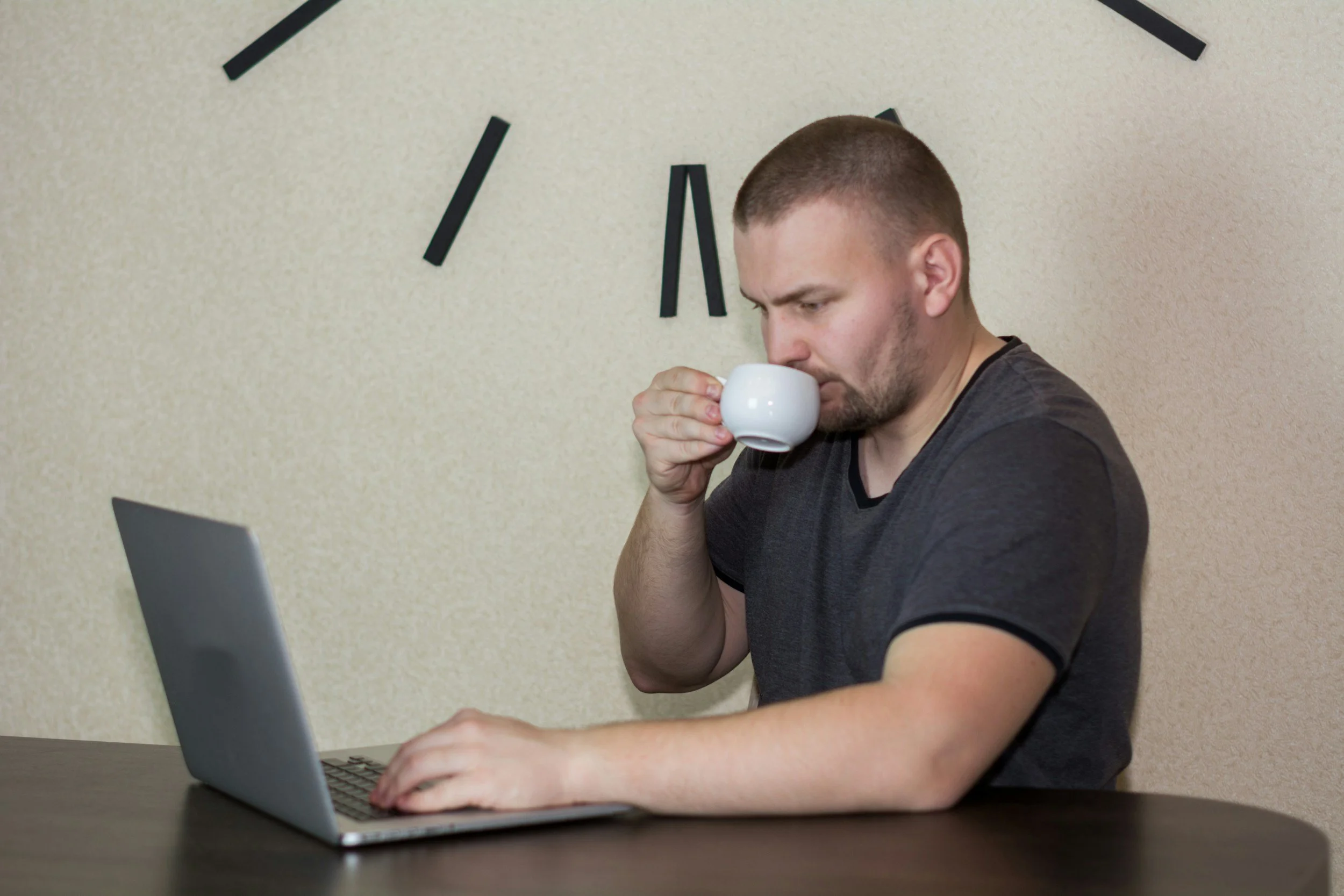 A desk worker sitting at his laptop, drinking a cup of coffee.